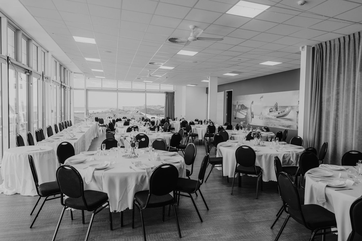 Elegant banquet hall with round tables set for a formal event, featuring large windows and classic black chairs.