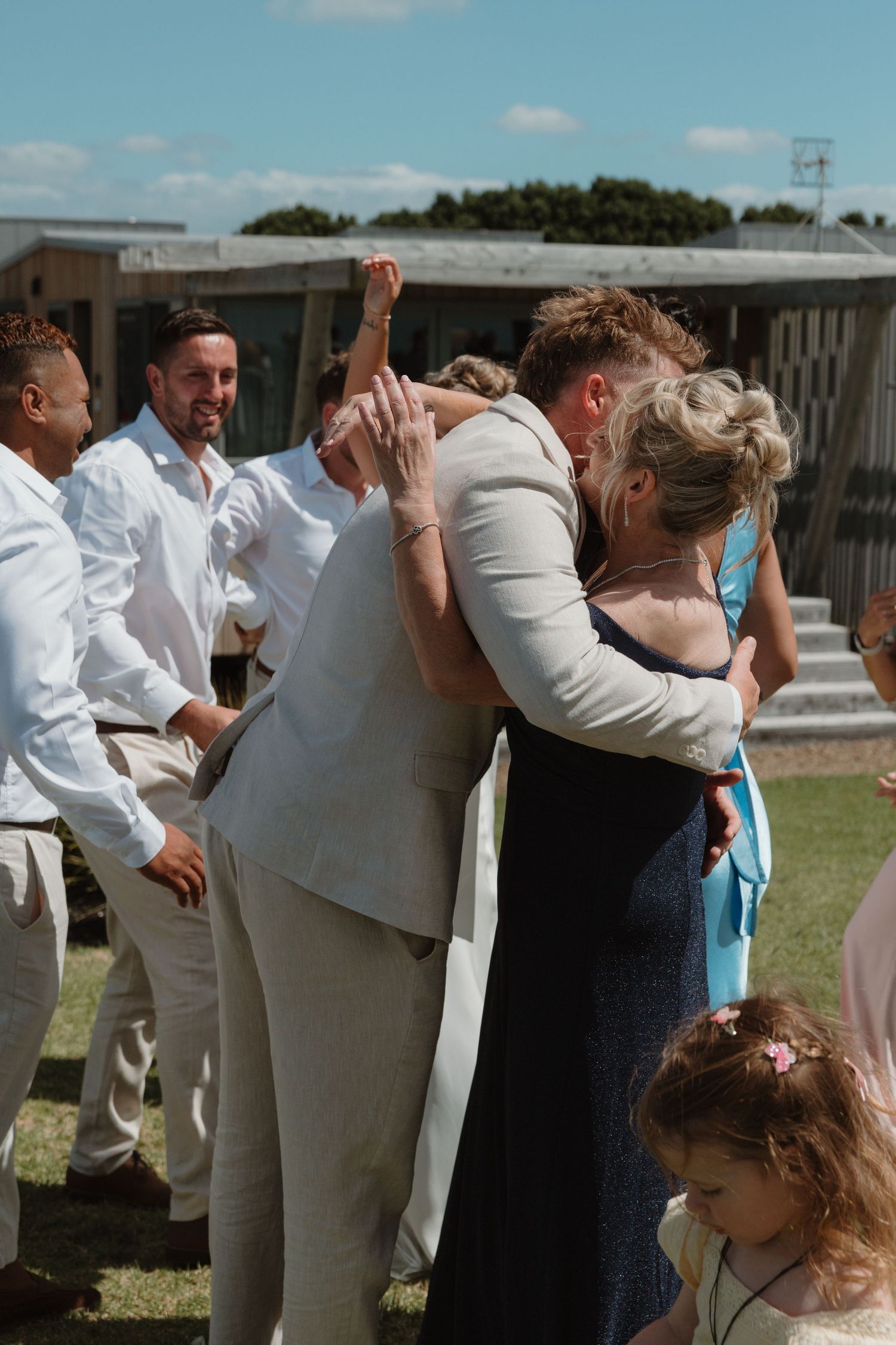 Guests sharing warm hugs and celebrating at an outdoor wedding reception on a sunny day.