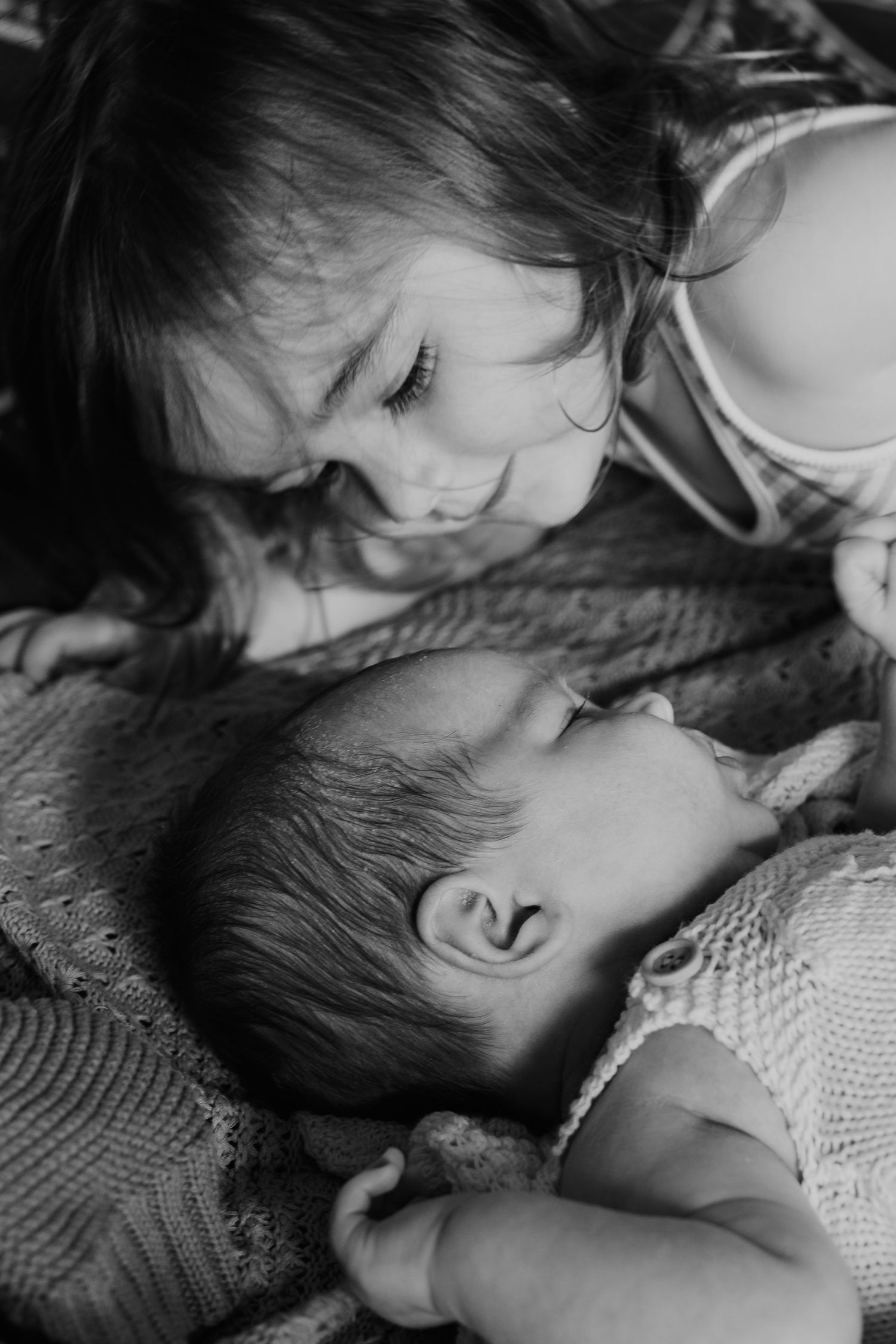 A gentle black and white portrait captures two children sharing a tender intimate moment while lying down together.