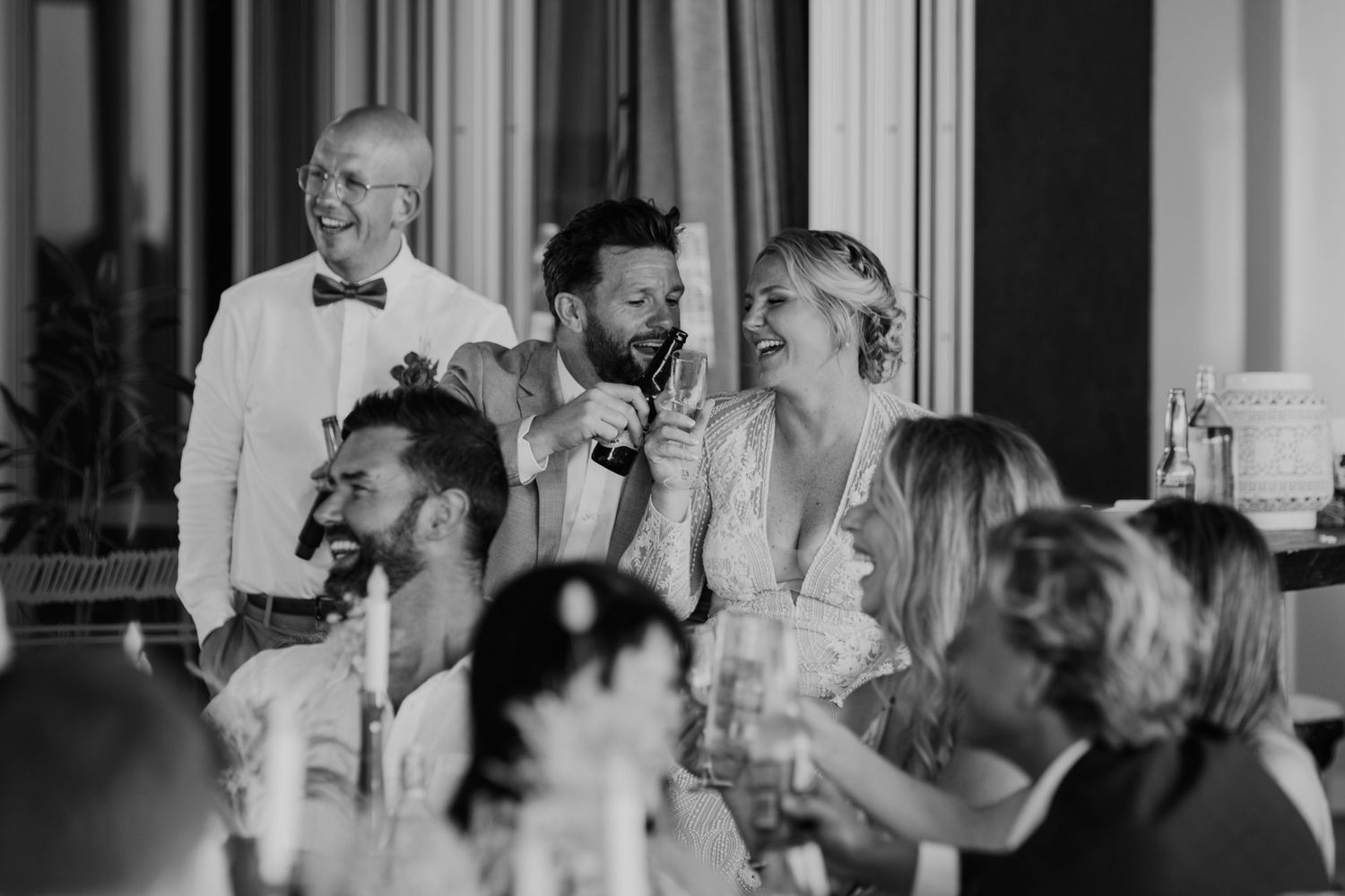 Black and white photo of wedding celebration showing guests laughing and enjoying themselves at a reception dinner.
