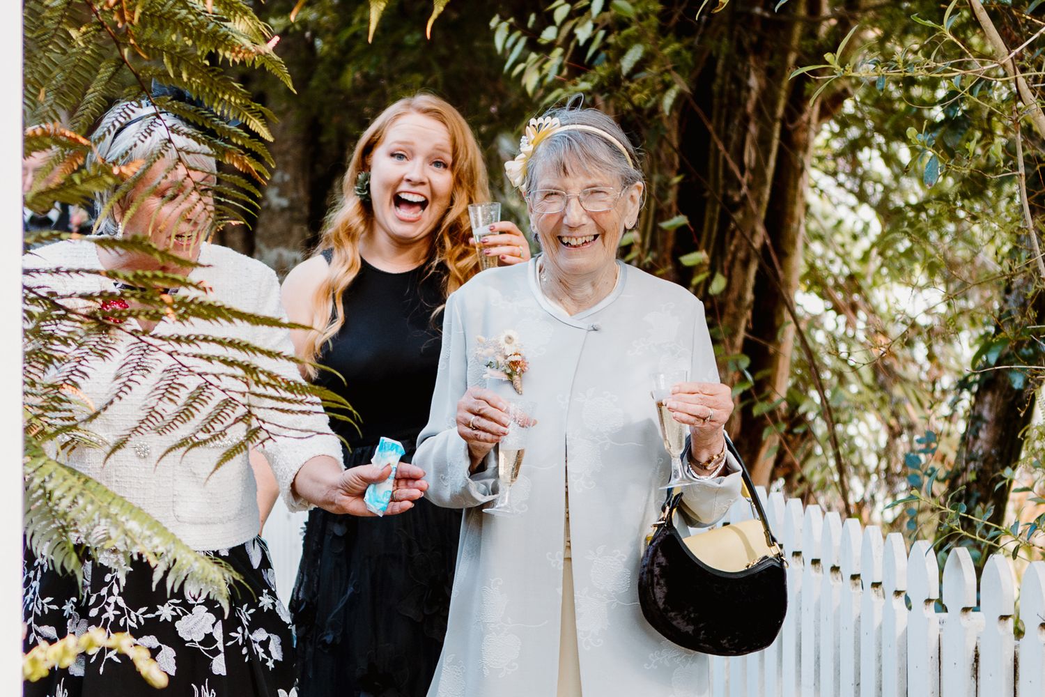 A joyful candid moment between people sharing wine outdoors in a garden setting during a celebration.