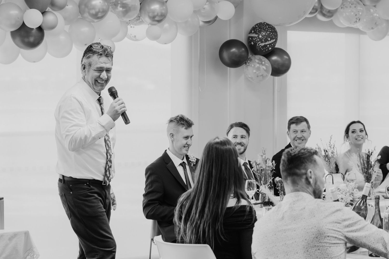 Guests celebrate at a wedding reception with festive hanging lights and decorations in an indoor venue.
