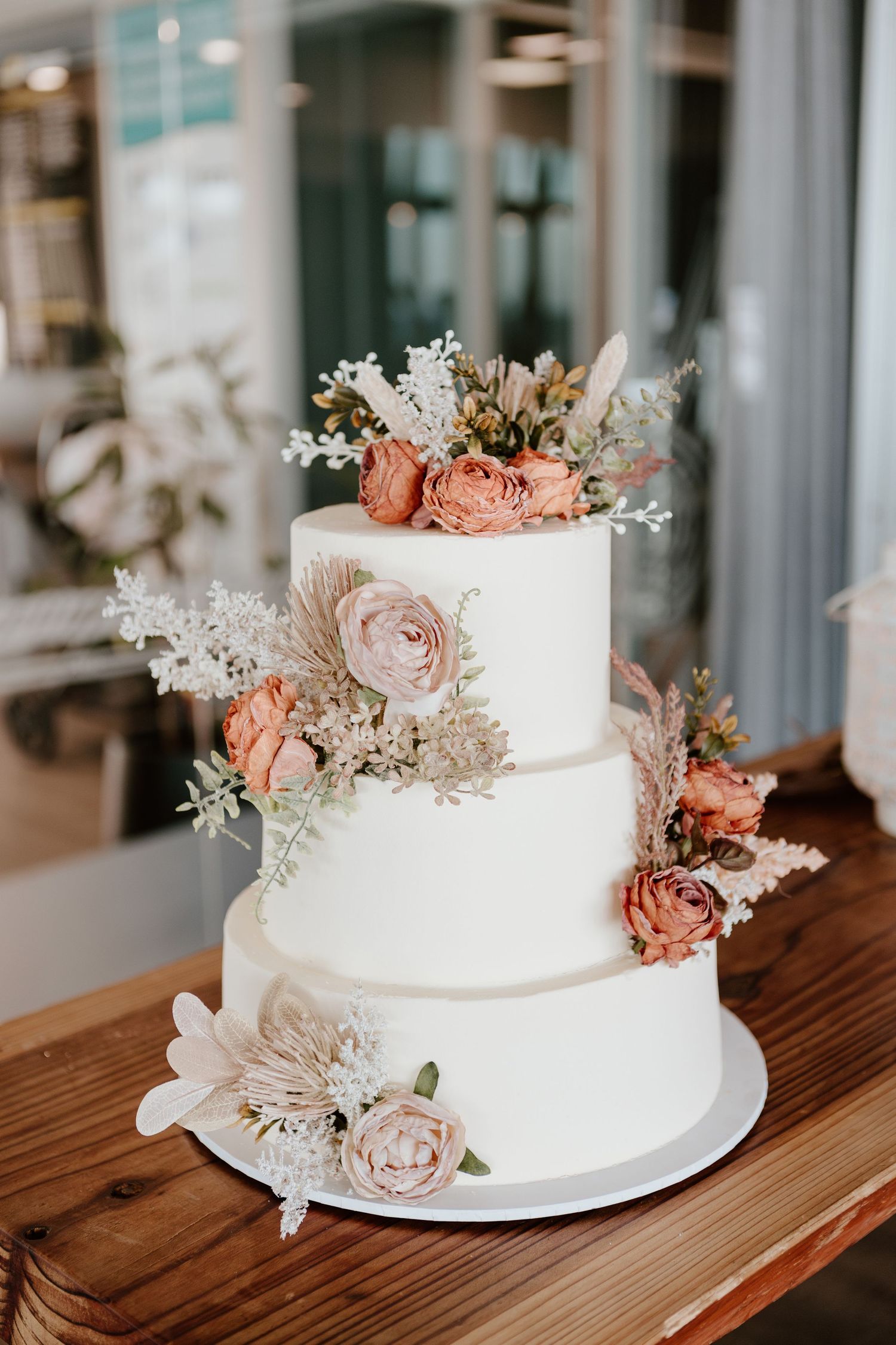 Elegant three-tier white wedding cake decorated with peach roses and delicate dried flowers. Papamoa Surf Lifesaving Club Wedding