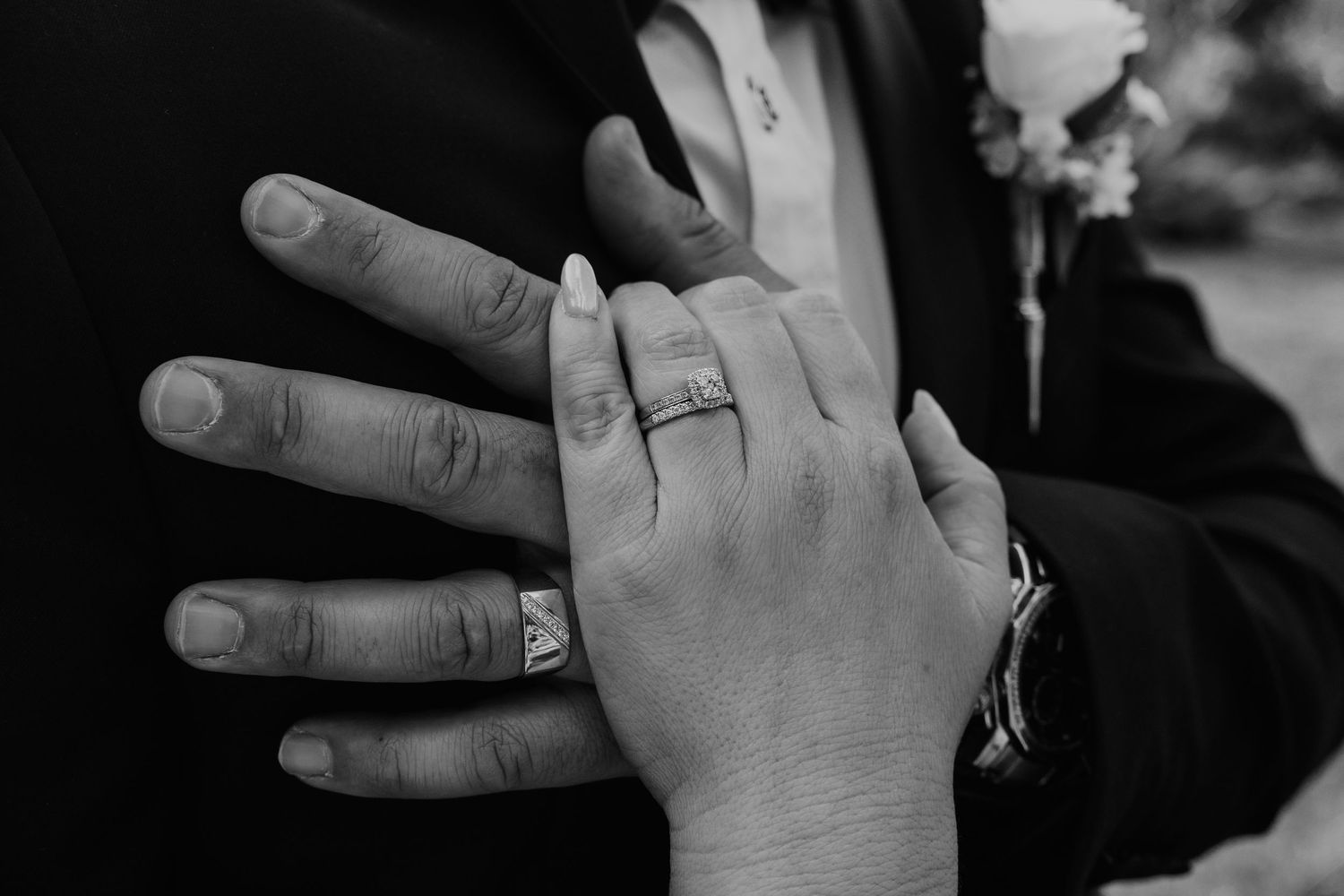 Black and white close-up of two hands with wedding rings touching intimately.