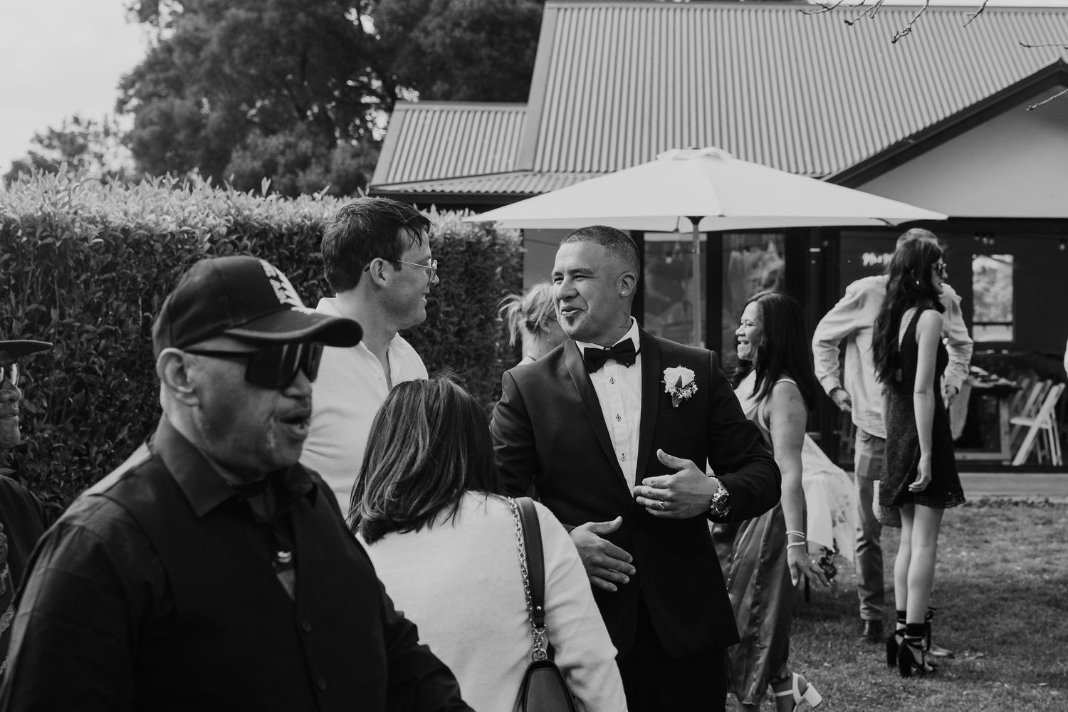 Black and white photo of guests socializing at an outdoor event with a barn or rustic building in the background.