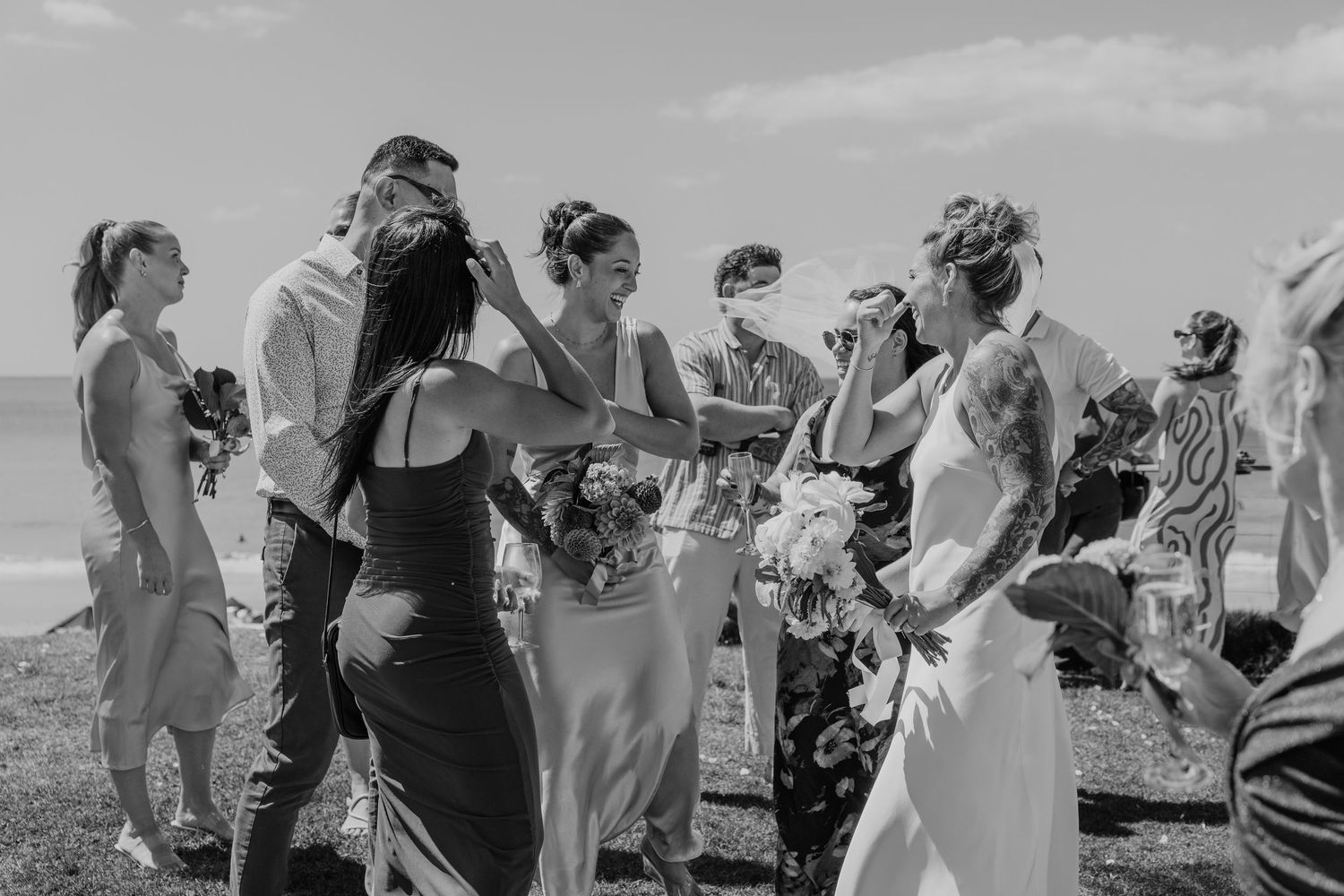 Black and white photo of wedding guests congratulating the bride outdoors near the ocean.