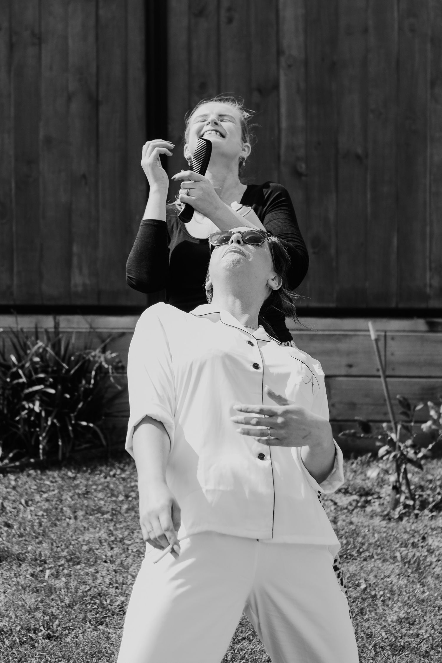 A black and white photo of two people in casual attire laughing and posing playfully outdoors.