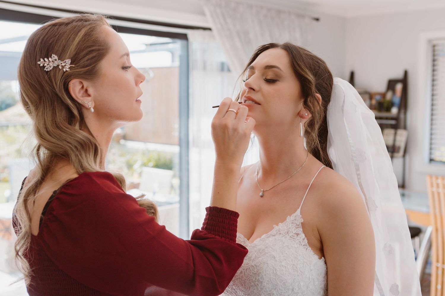 Two figures in burgundy and white attire sharing a close moment during a formal event preparation.