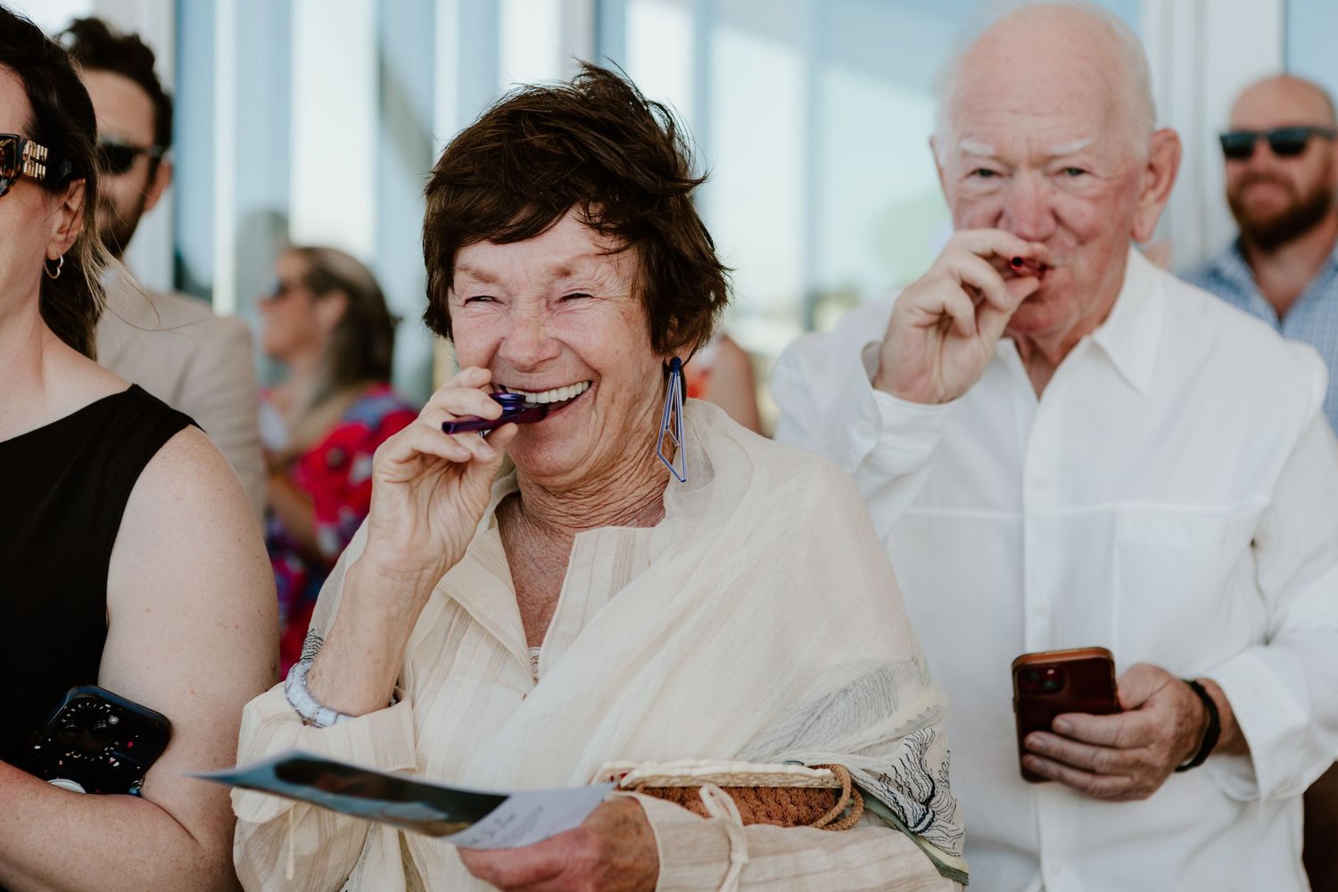 A group of guests laugh heartily while enjoying refreshments at an outdoor event.