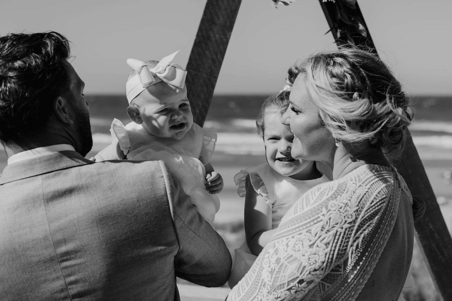 An intimate moment shared during a beach wedding ceremony under a wooden arch.  Papamoa Surf Lifesaving Club Wedding