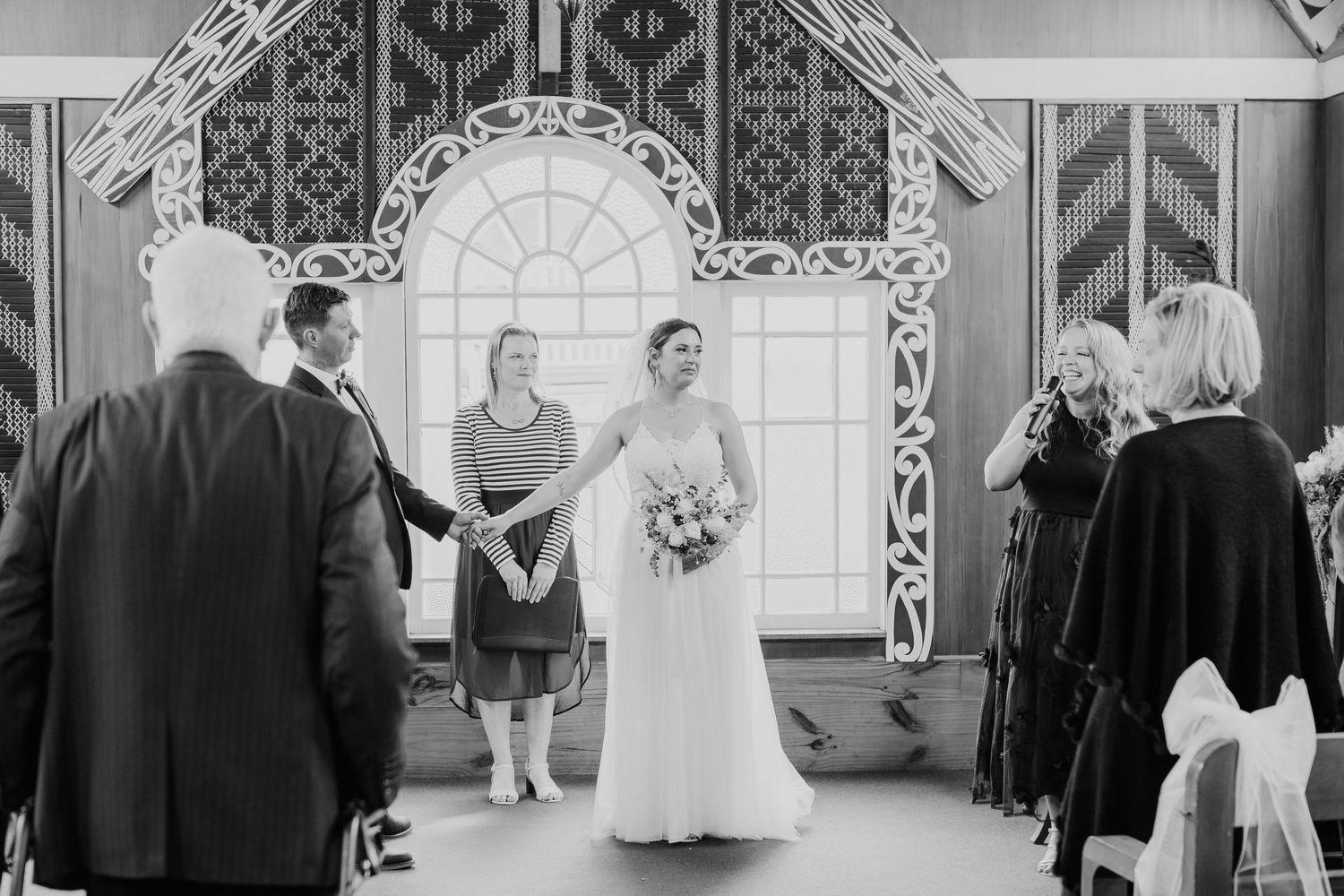 Wedding ceremony scene with ornate white archway and geometric patterns in background.