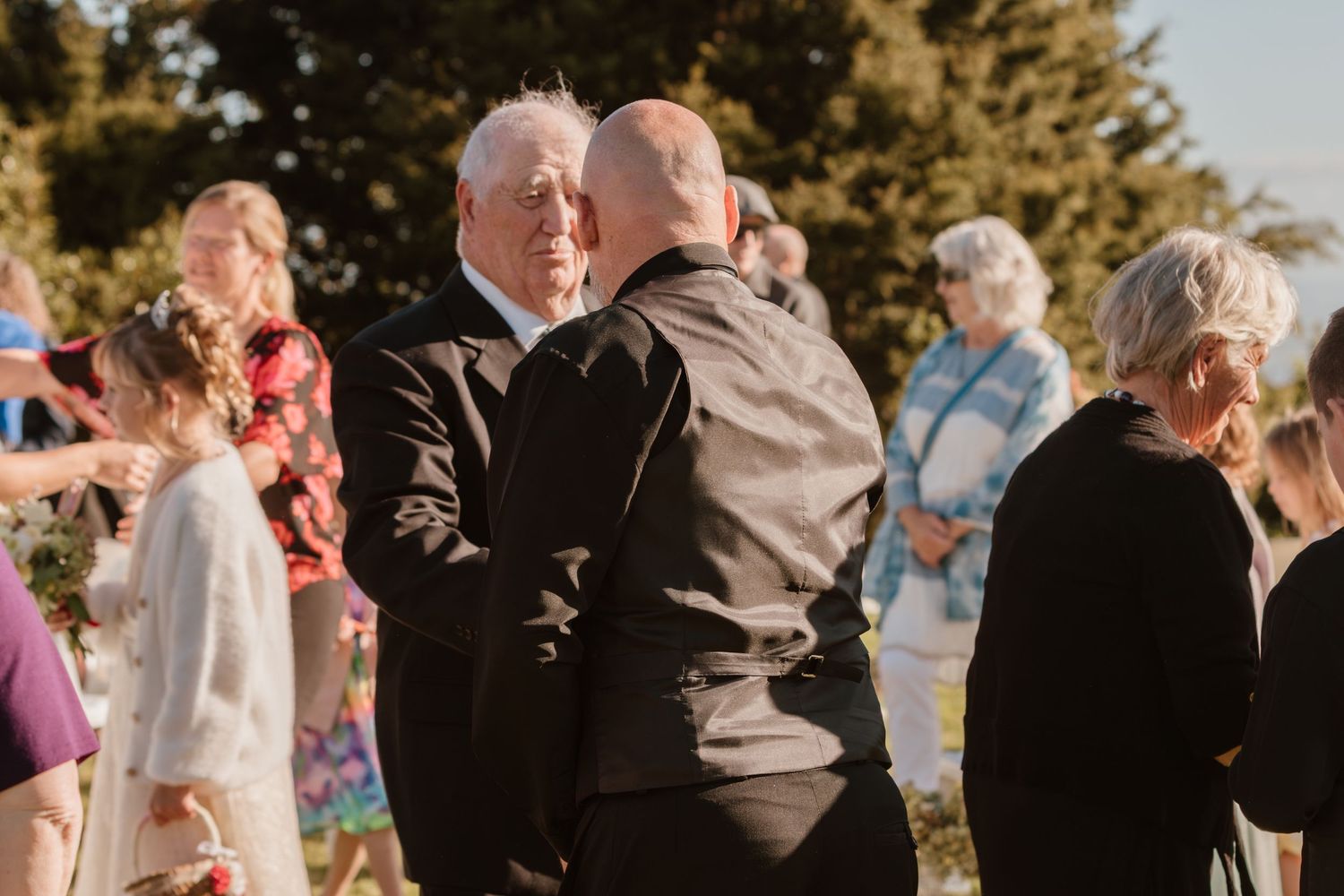 A warm outdoor gathering with people embracing during a sunset celebration in a garden setting.