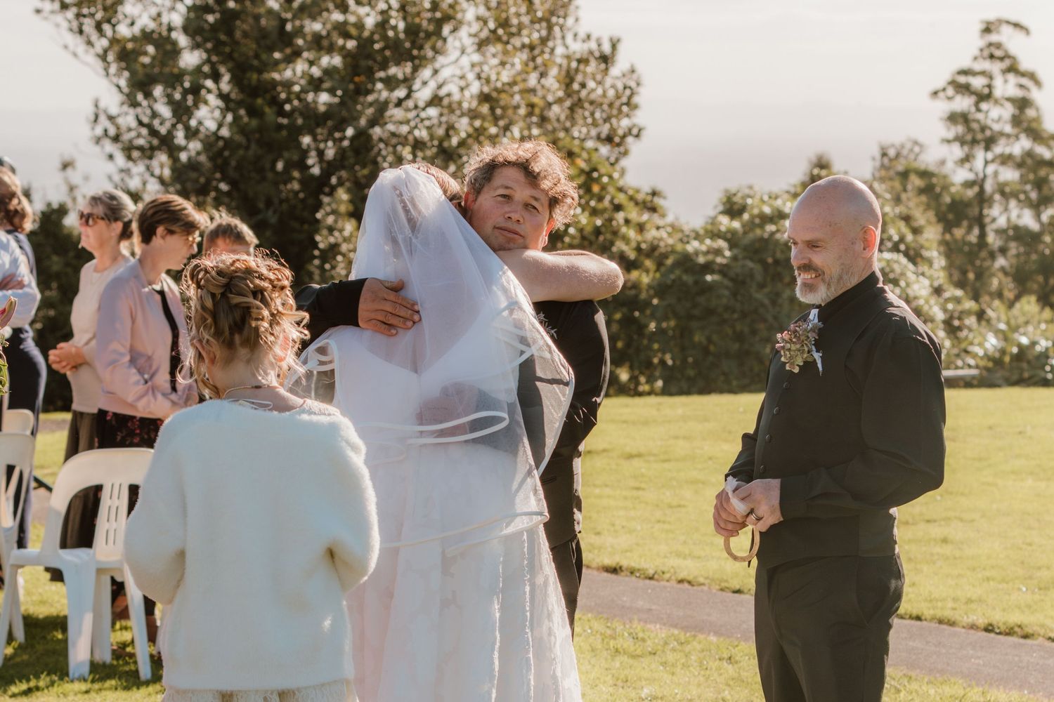 Wedding guests gather outdoors on a sunny day during an emotional celebration at a scenic hilltop venue.
