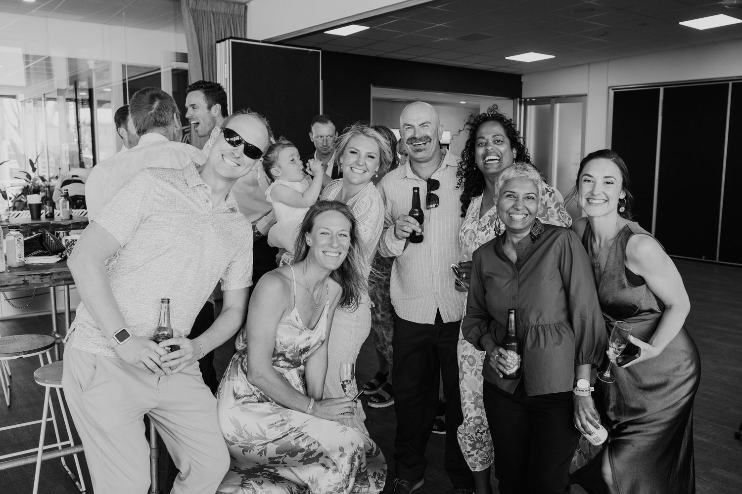 A group of people gathered together at an indoor event celebrate and pose for a black and white photograph.