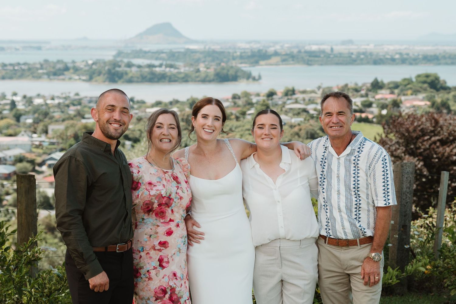Group of five people smiling outdoors at a wedding with scenic lake and mountain views in the background.