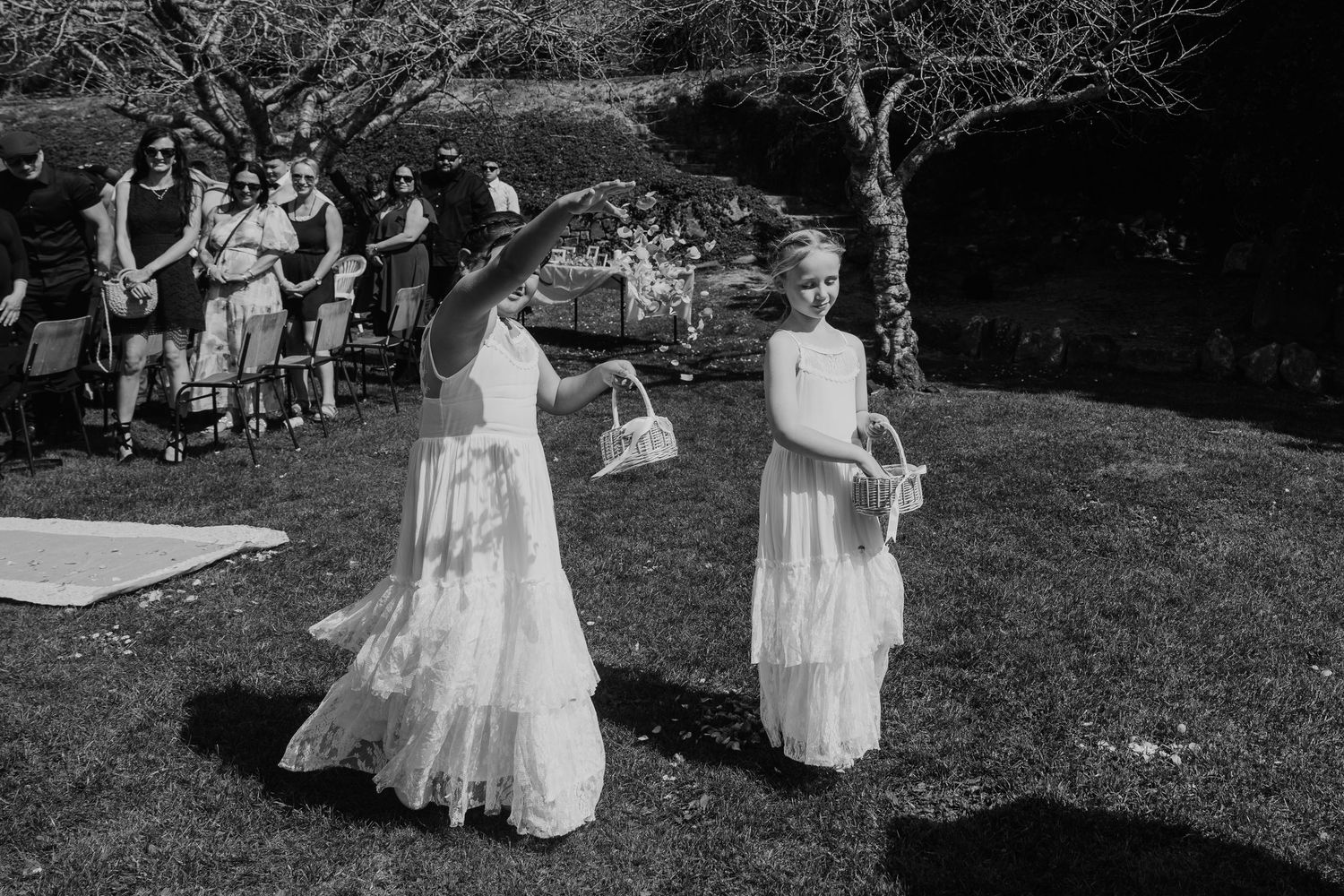 A couple shares a romantic dance outdoors in a garden setting while guests watch from the sidelines.