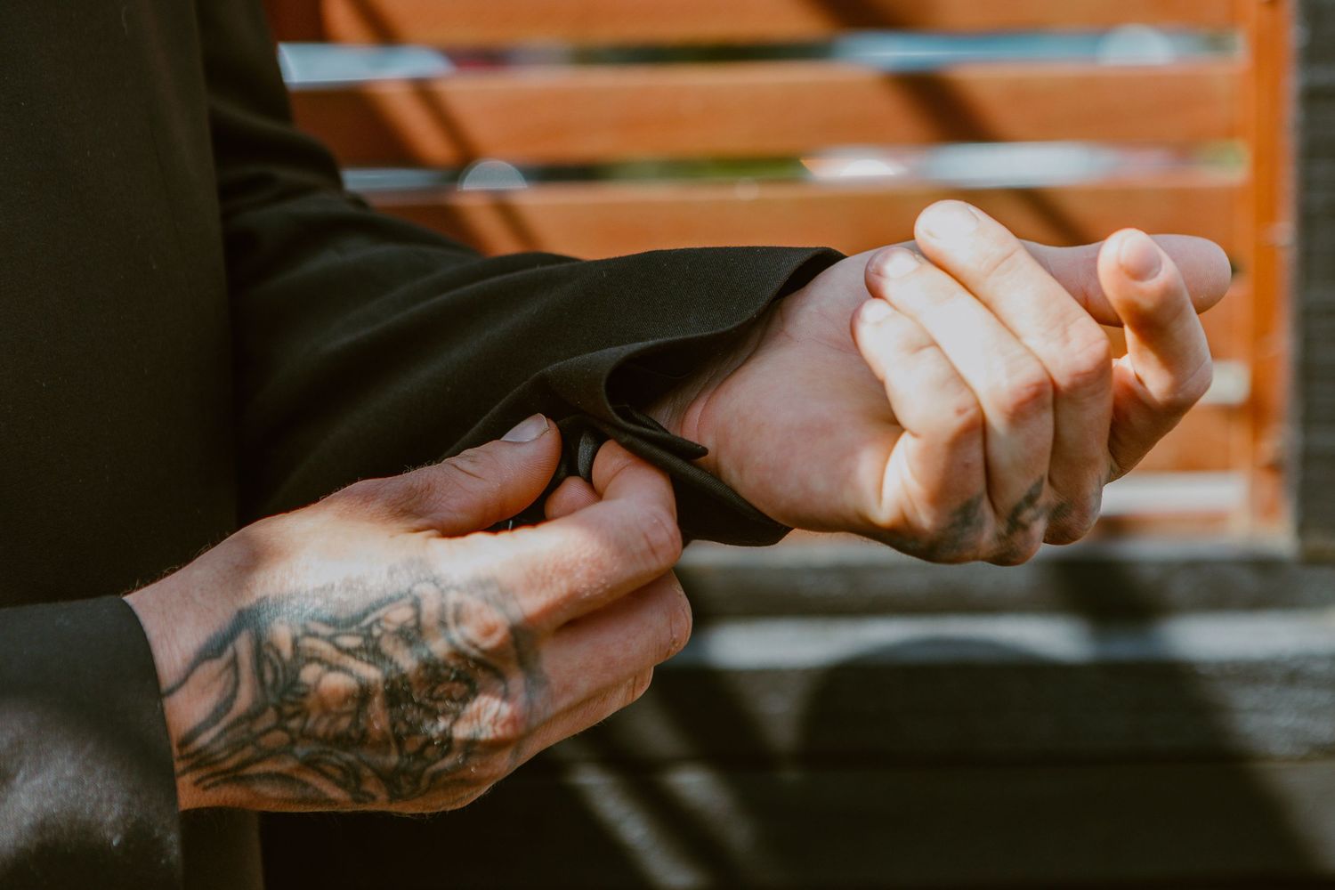 Groom in black suit tying formal dress shoes while sitting on wooden deck.