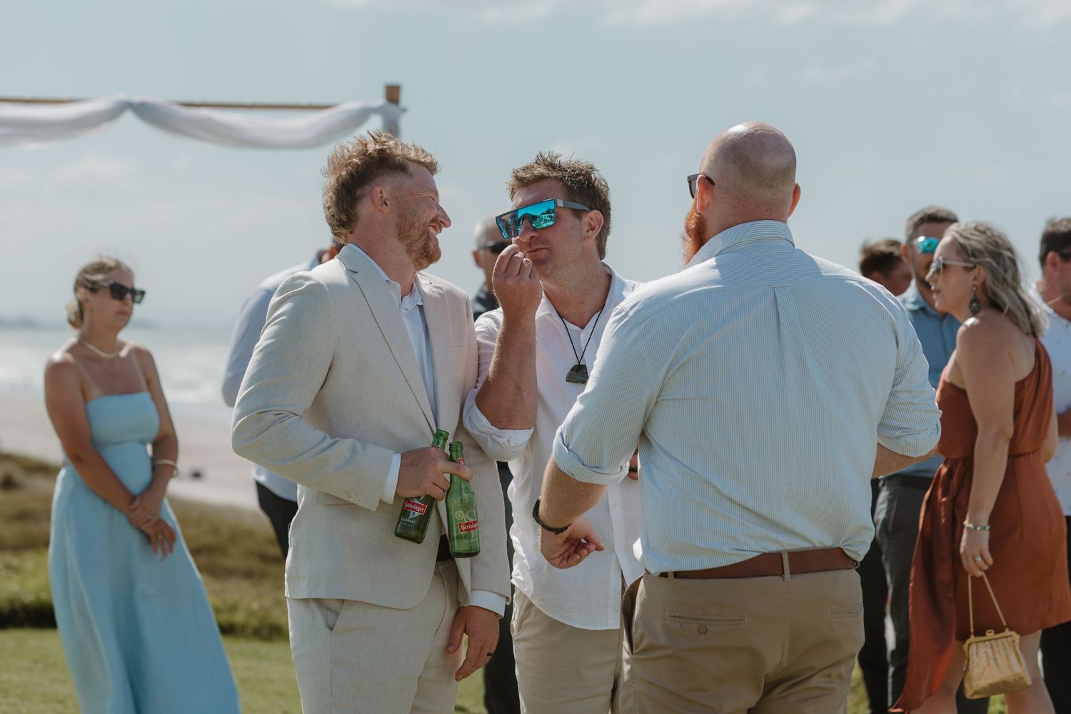 Guests mingling outdoors at a beachside wedding reception on a sunny day.
