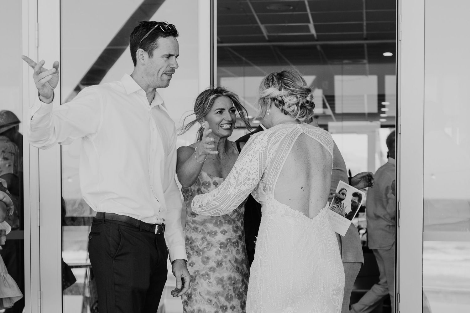 Wedding guests hugging and celebrating with genuine emotion in an indoor venue. Papamoa Surf Lifesaving Club Wedding