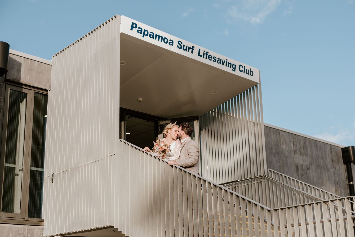 A couple poses at the Copacabana Surf Lifesaving Club building entrance during their wedding. Papamoa Surf Lifesaving Club Wedding