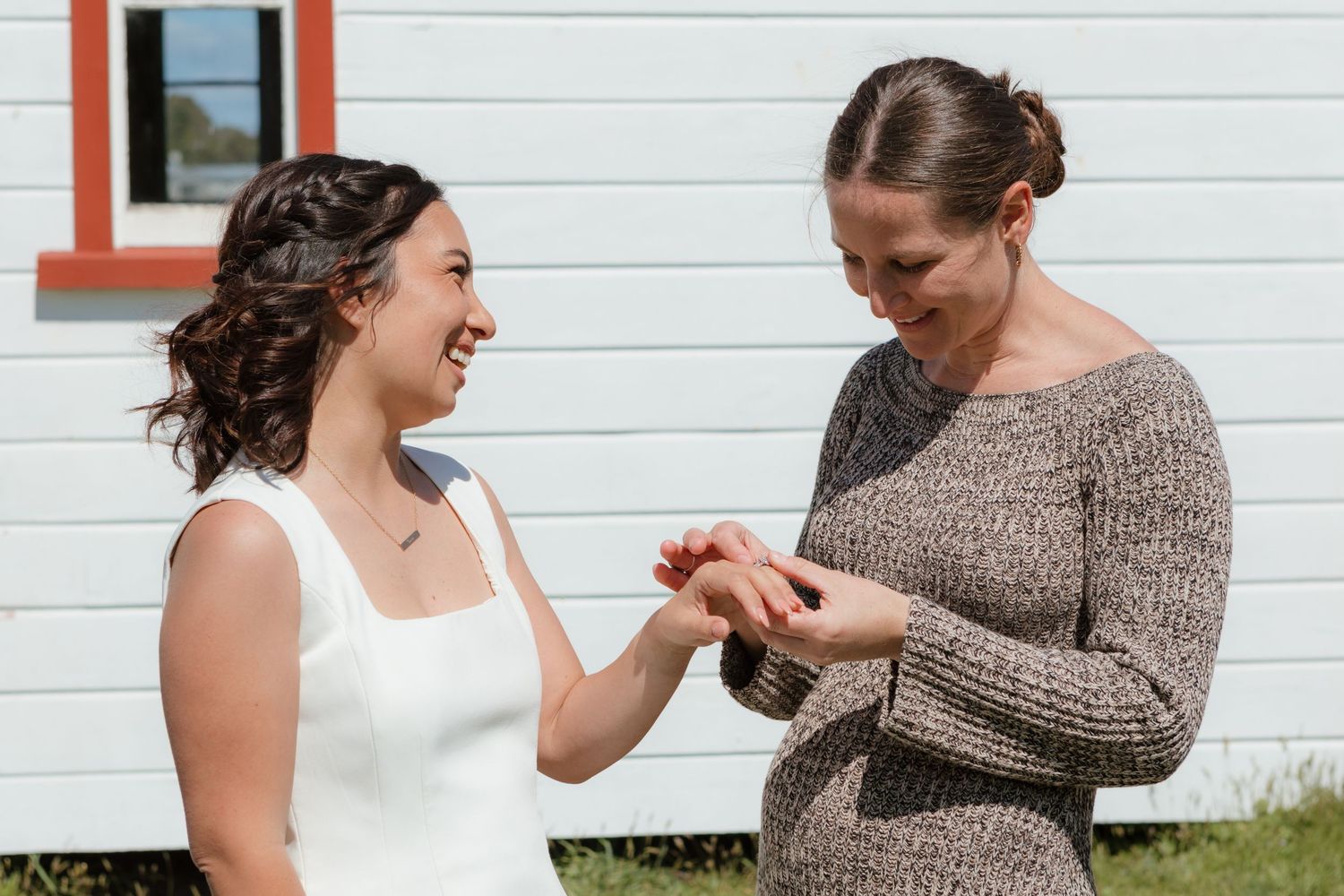 Two people stand together outdoors examining rings in front of a white building with a small red window frame.