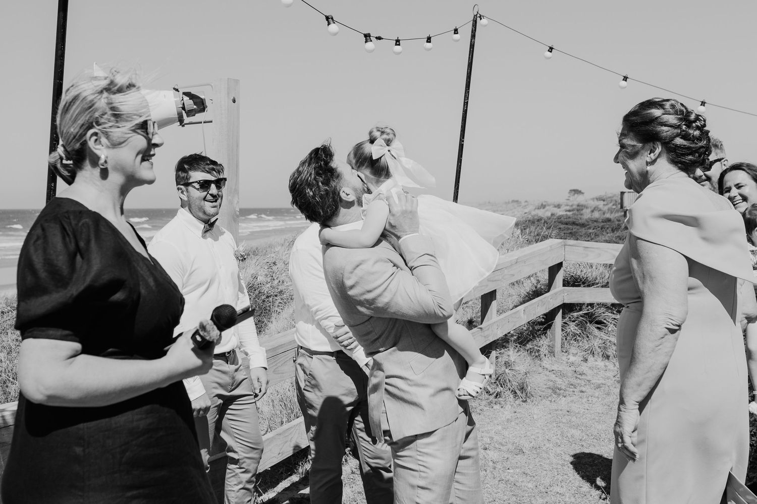 A vintage black and white photo shows a casual outdoor group gathering with people interacting under strung lights.