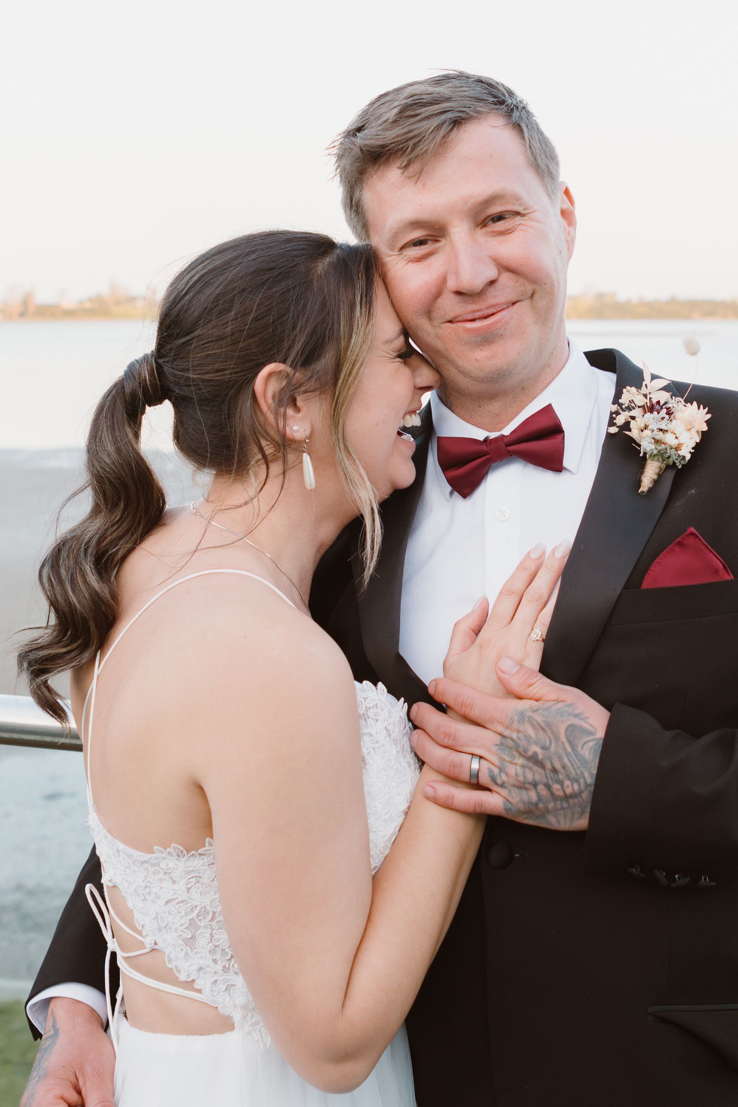 Happy newlyweds in wedding attire share intimate moment outdoors at sunset.