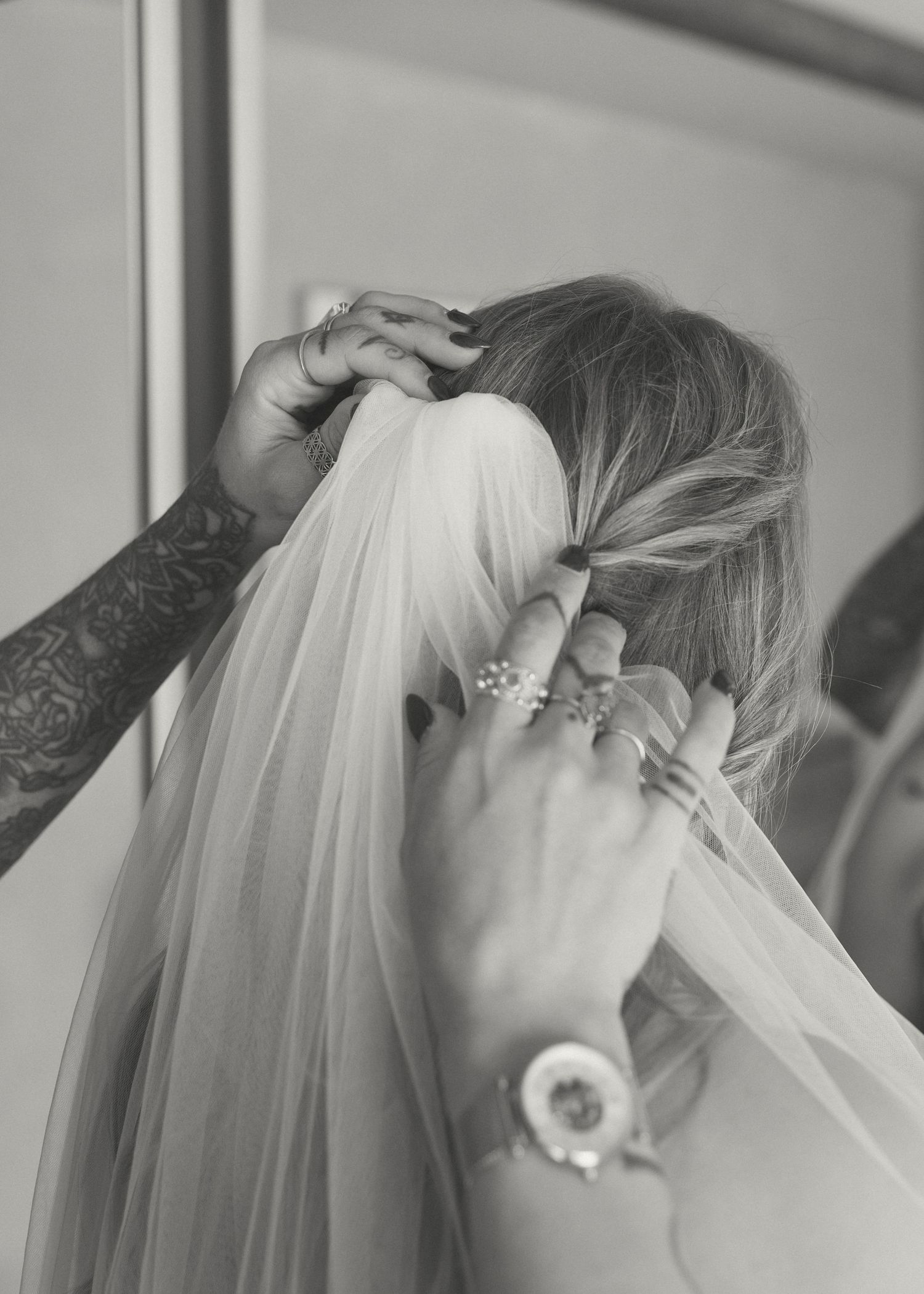 Tattooed hands placing a bridal veil into a blonde bride's braided updo hairstyle.