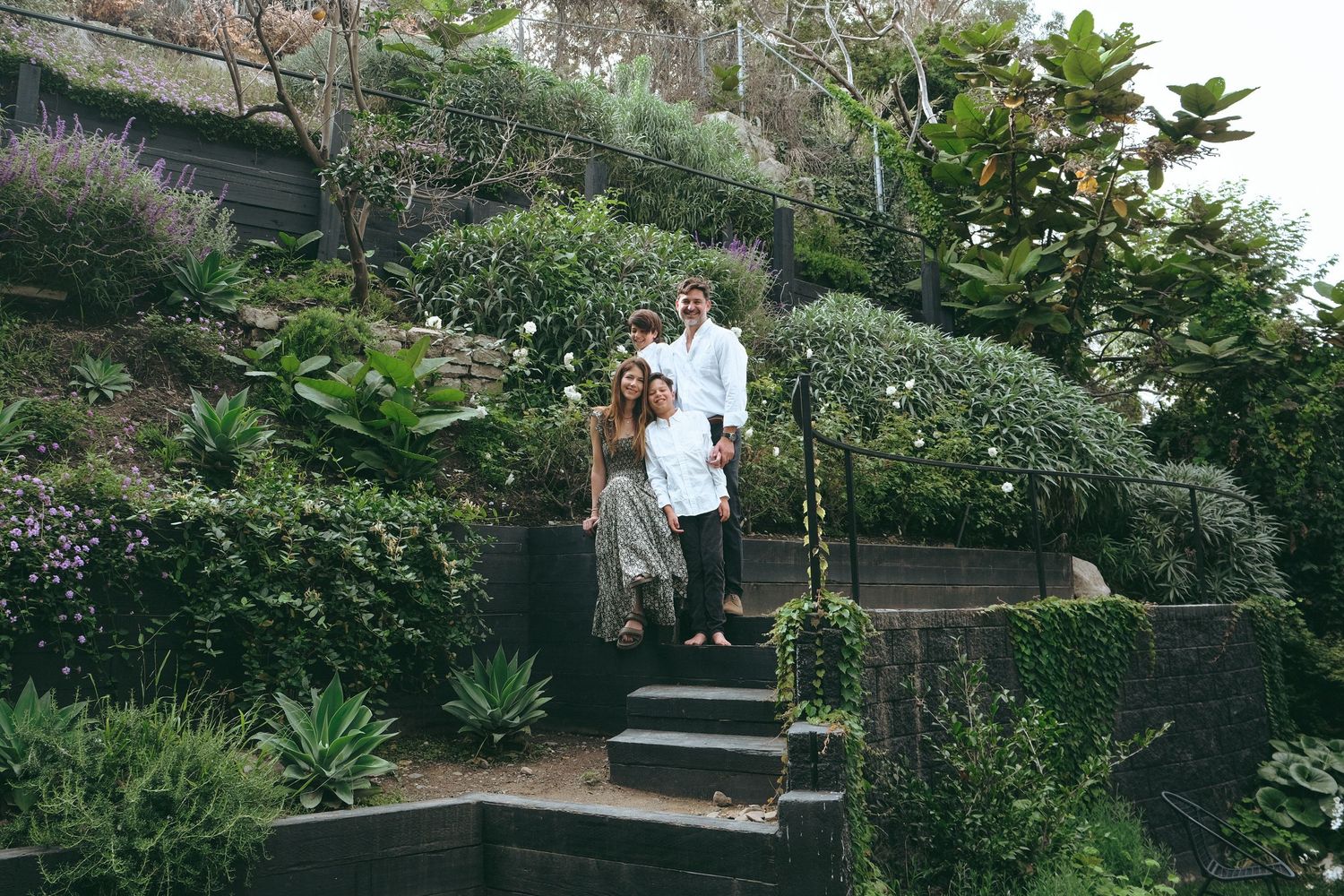 Family gathering in terraced garden with stone steps and tropical plants.