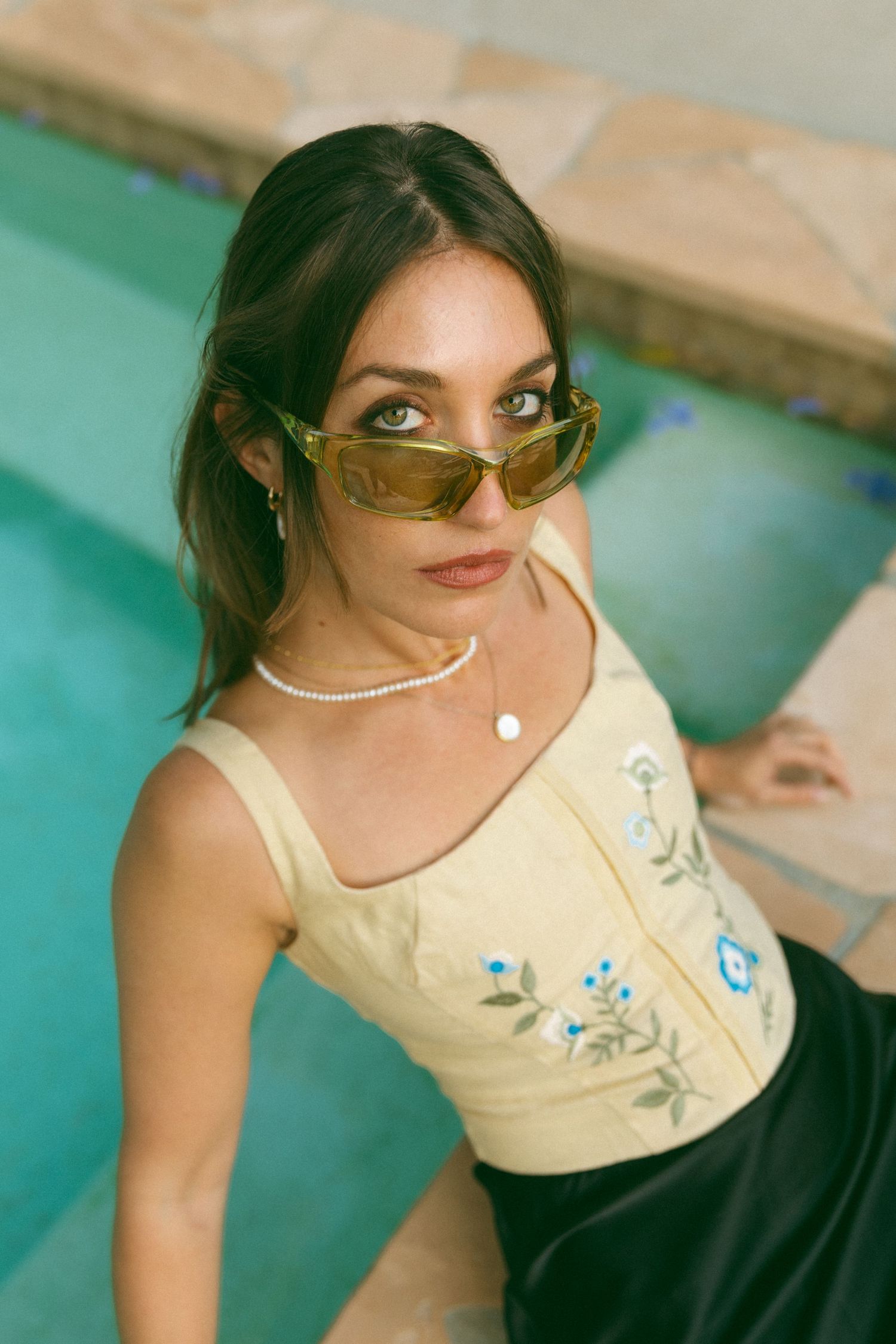 Vintage-inspired fashion portrait featuring yellow floral top and statement sunglasses by pool.