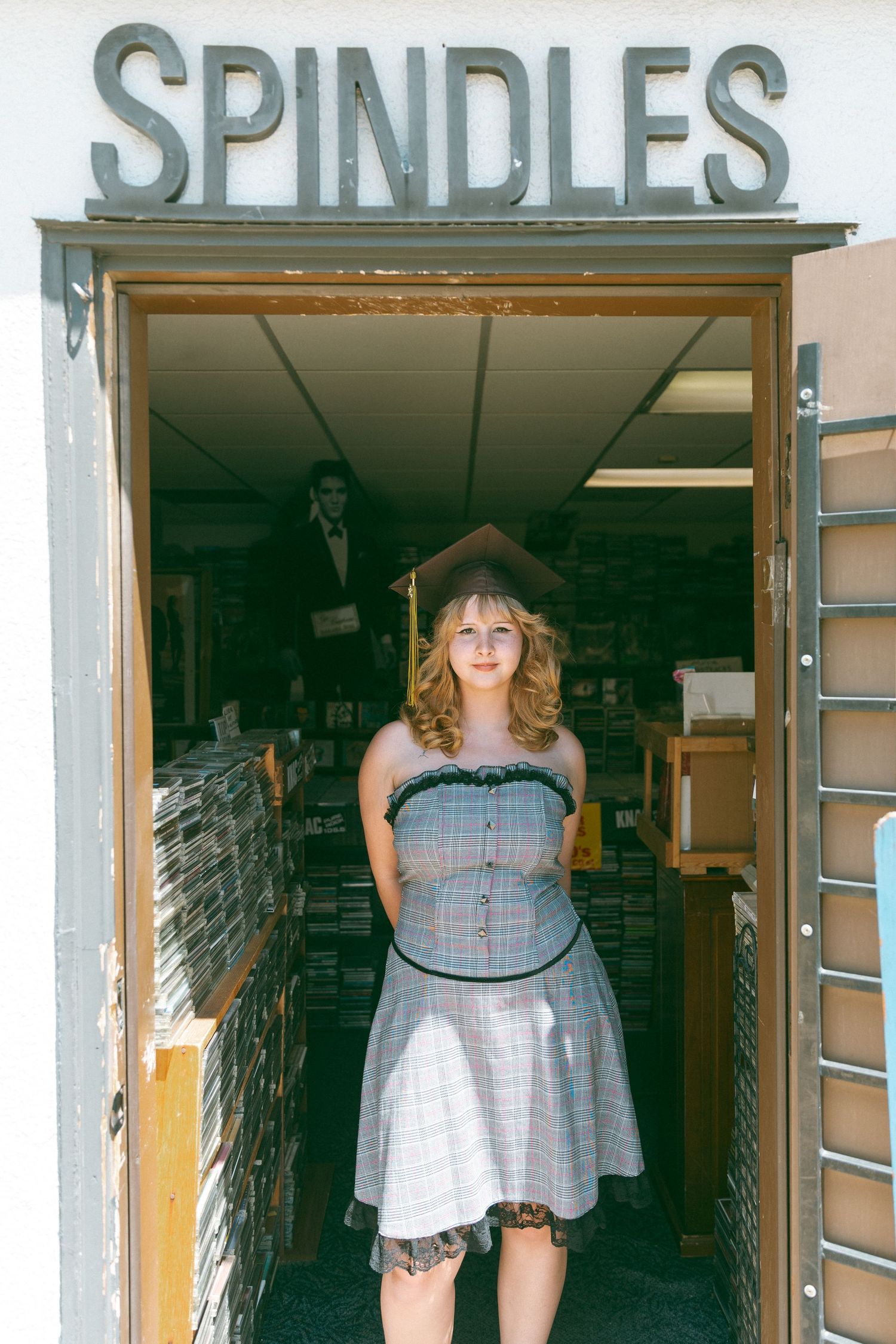 A person poses in a gray dress at the entrance of Spindles record store.