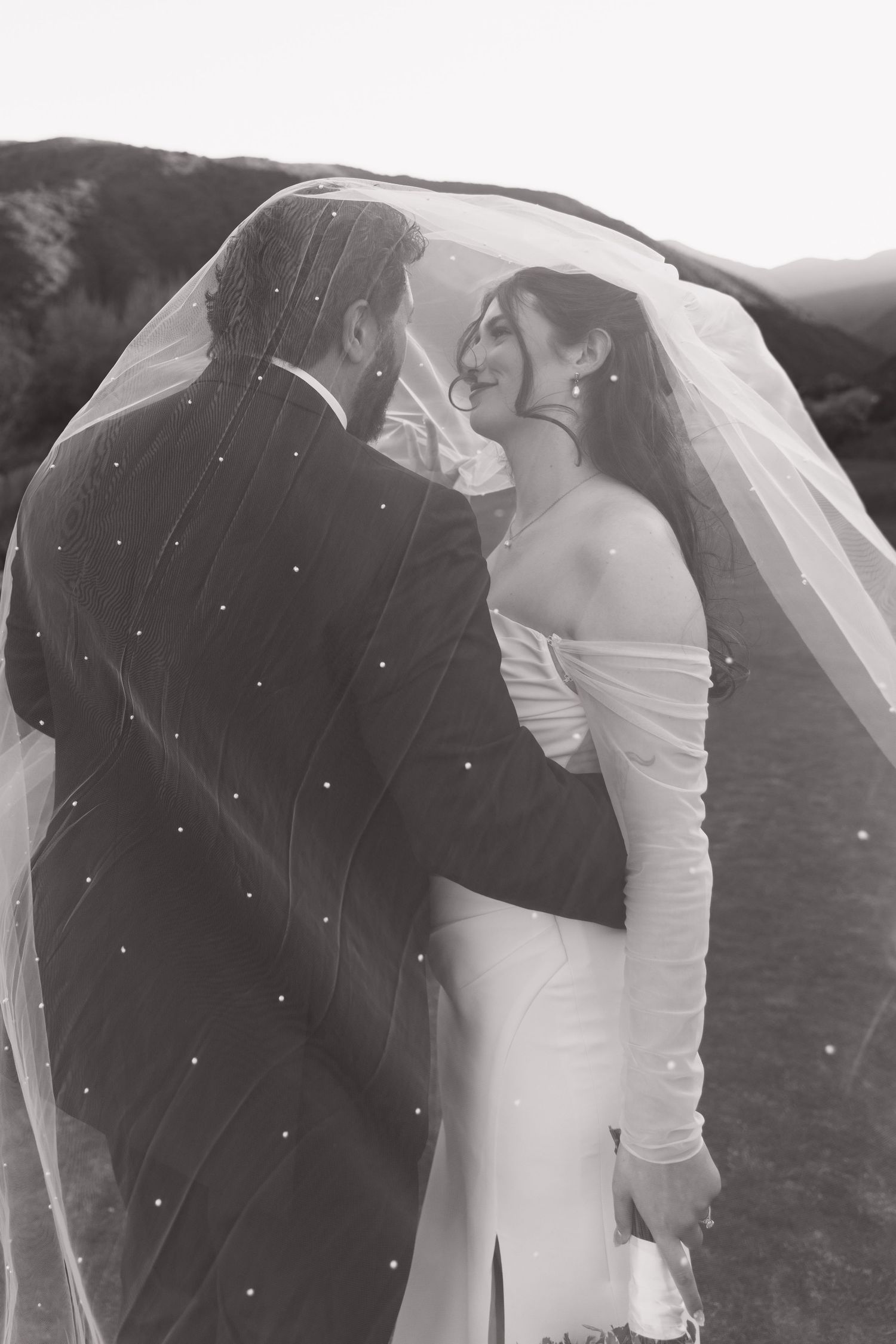 Romantic black and white portrait of newlyweds sharing intimate moment under bridal veil.