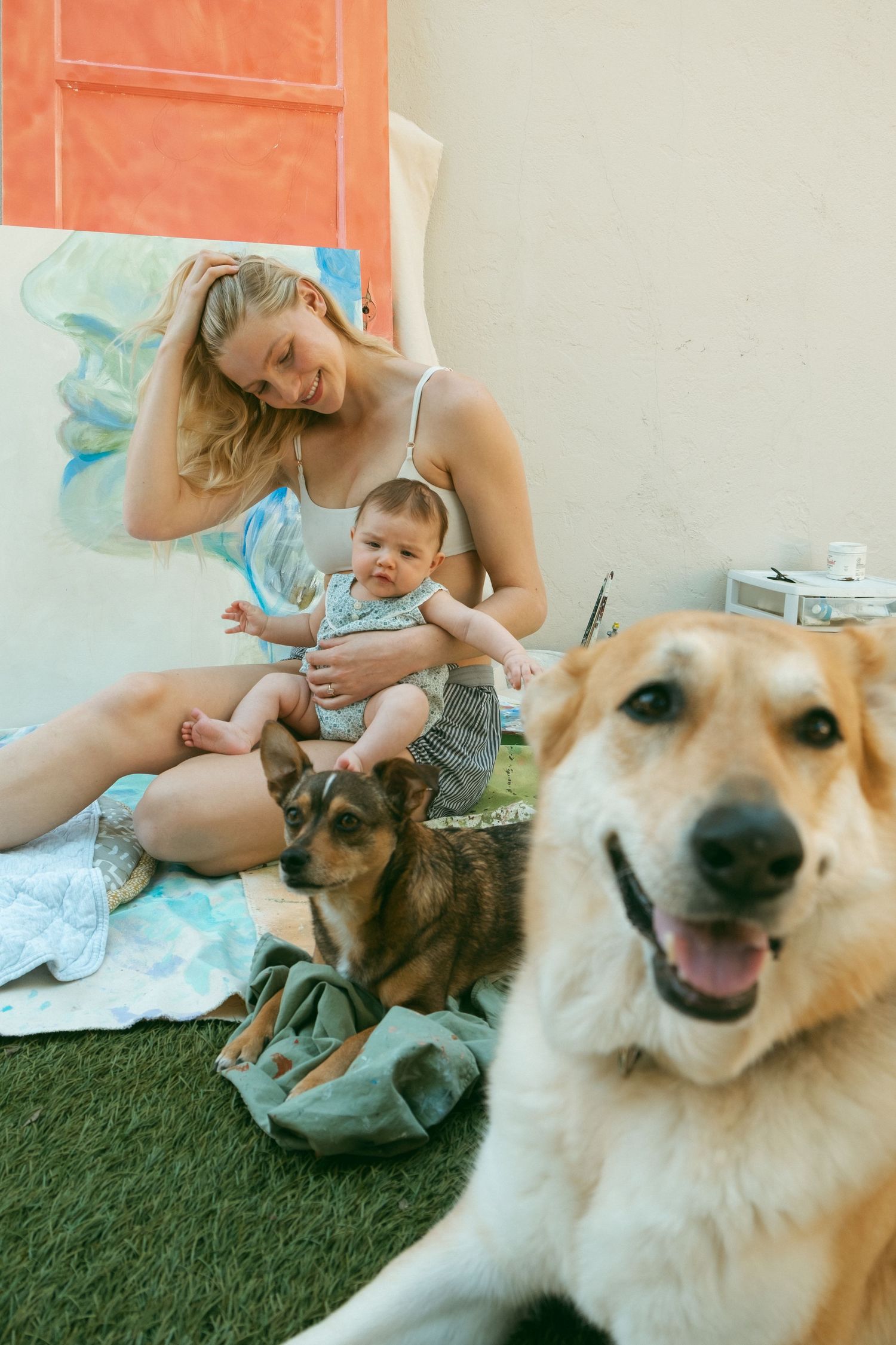 A heartwarming family moment with two dogs and a baby sitting on a blue blanket outdoors.