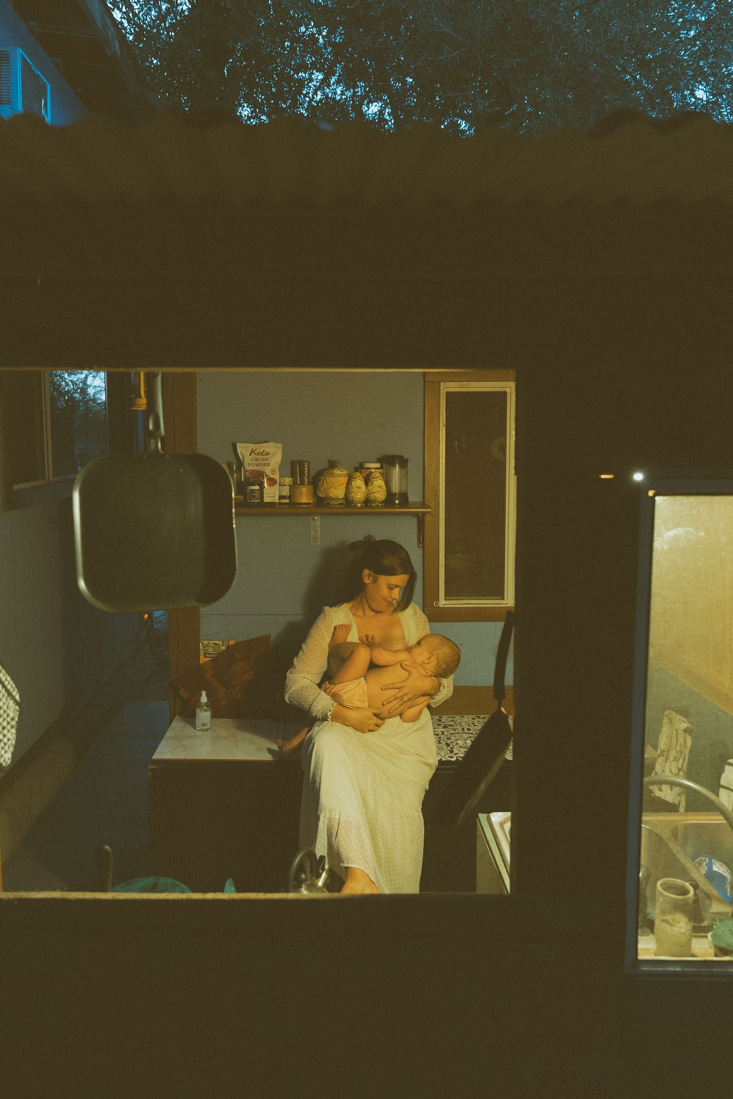Quiet moment between parent and child viewed through window panes with kitchen shelves visible.