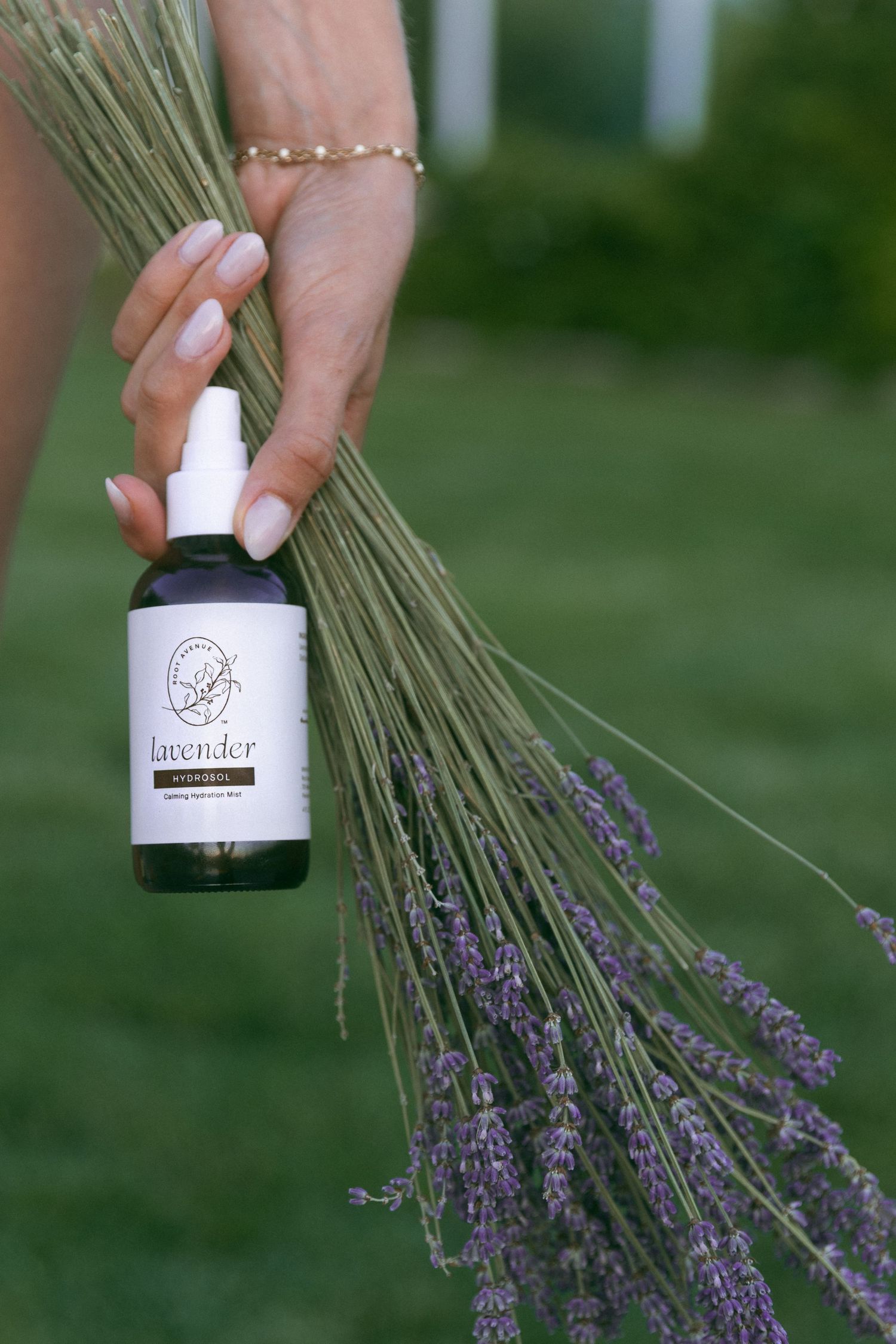 Hand holding a small bottle of essential oil product alongside fresh lavender stems.