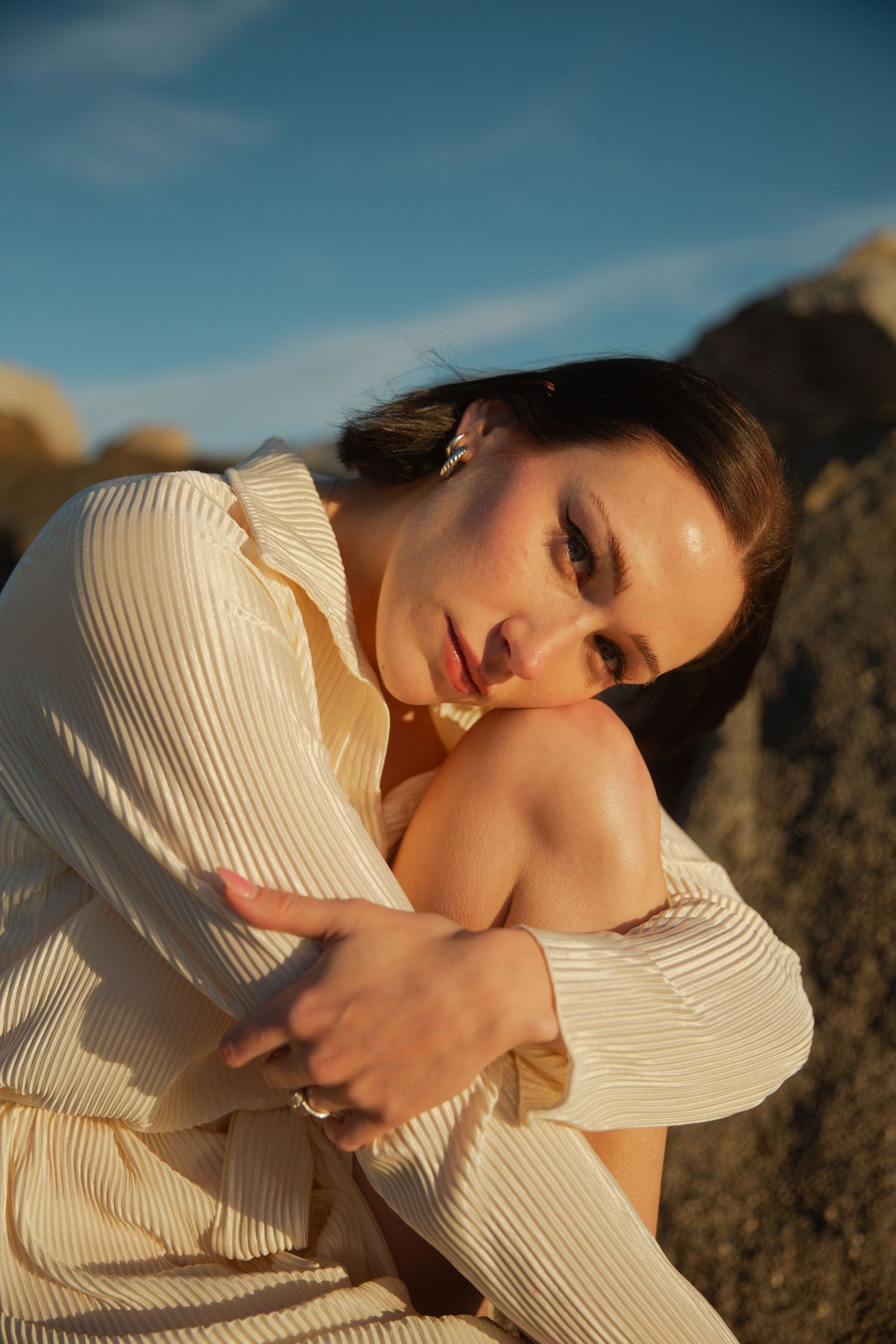 Figure in cream ribbed sweater poses dramatically against coastal rocks.