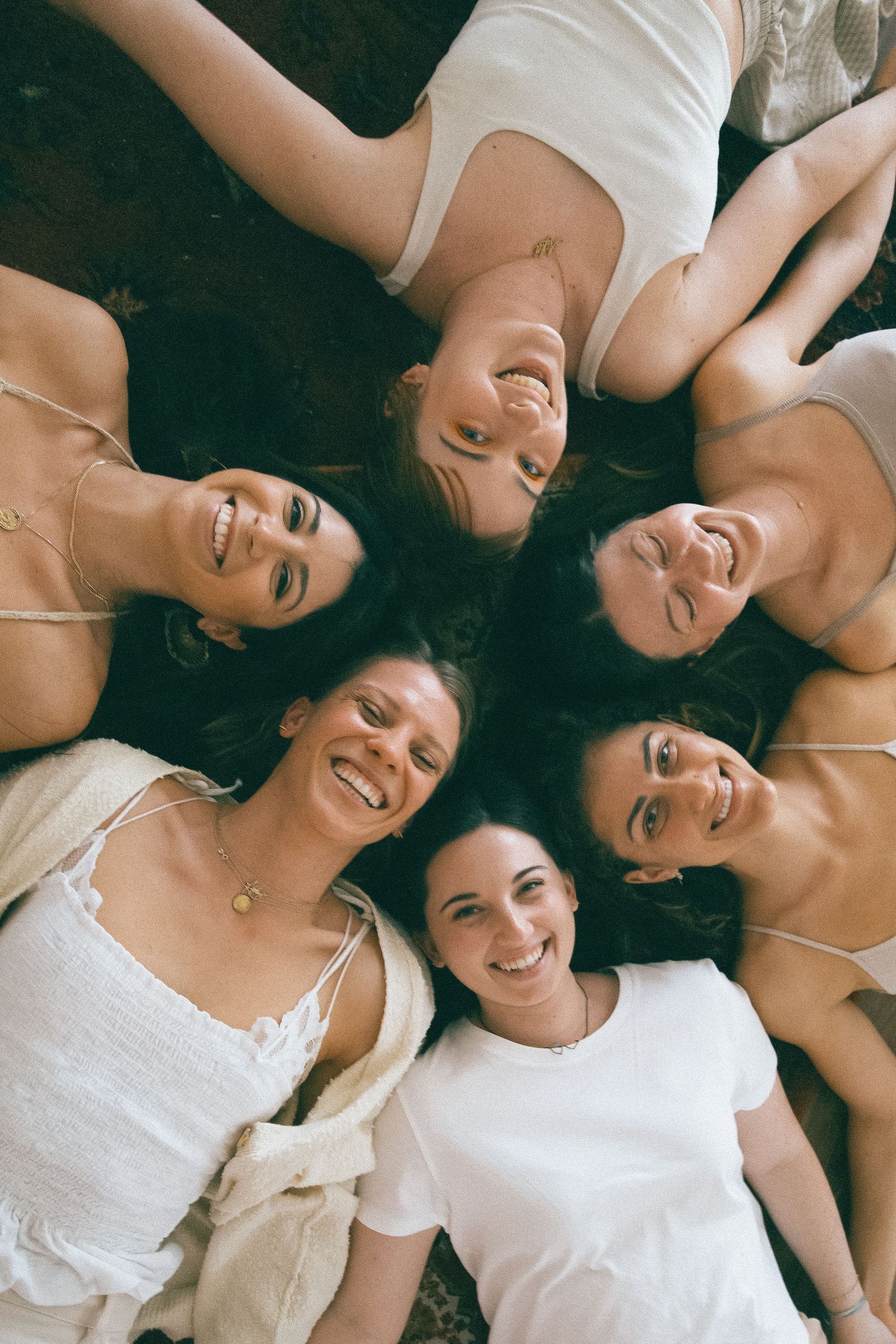 Friends lying down together in white tops smiling and laughing.