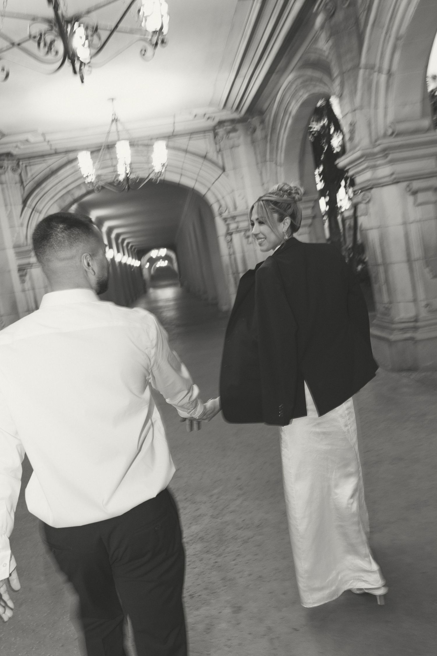 Wedding couple performing a dance sequence in an elegant hallway with classical architecture.