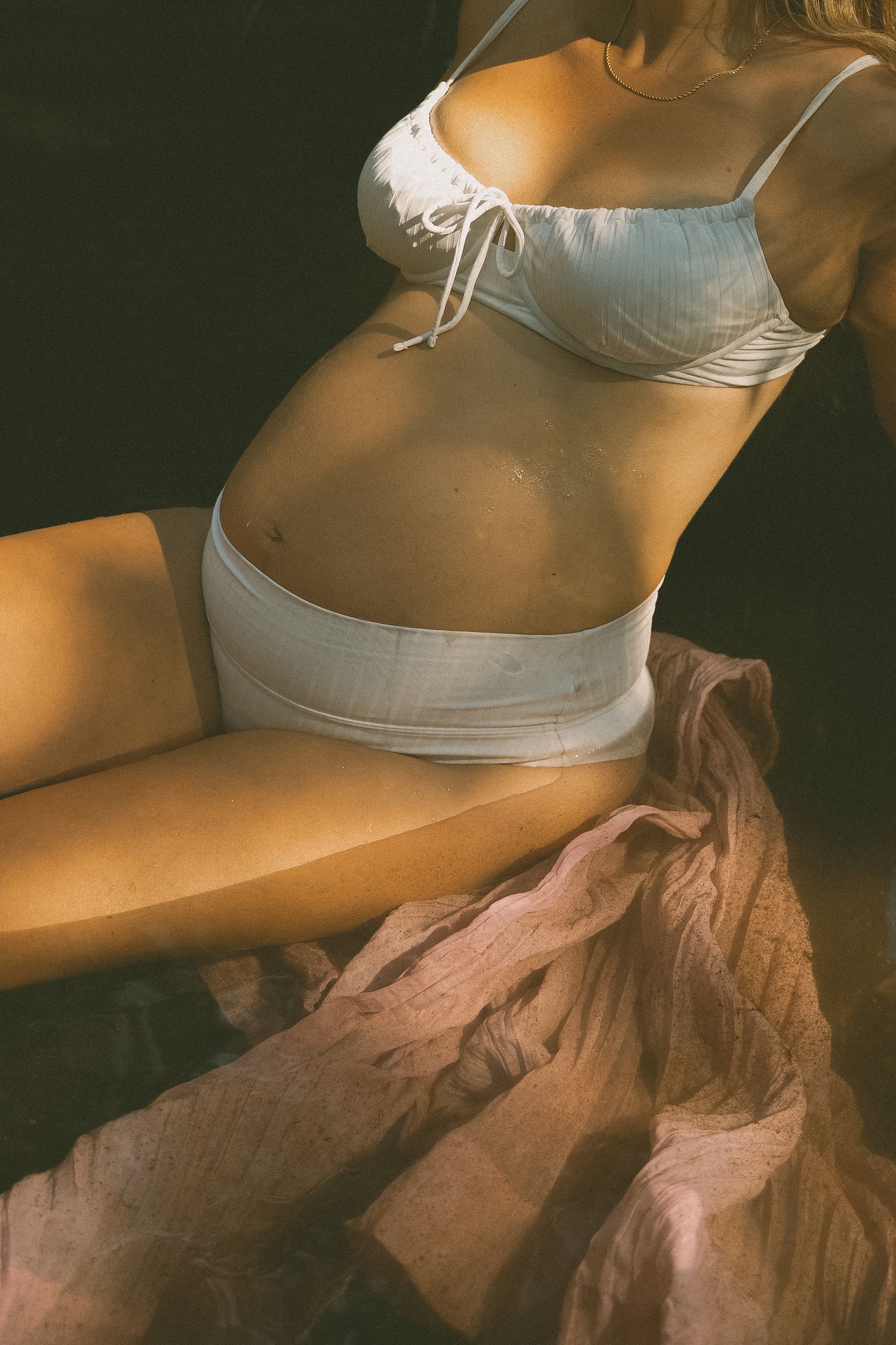 Intimate maternity portrait with white lingerie and flowing fabric in warm lighting.