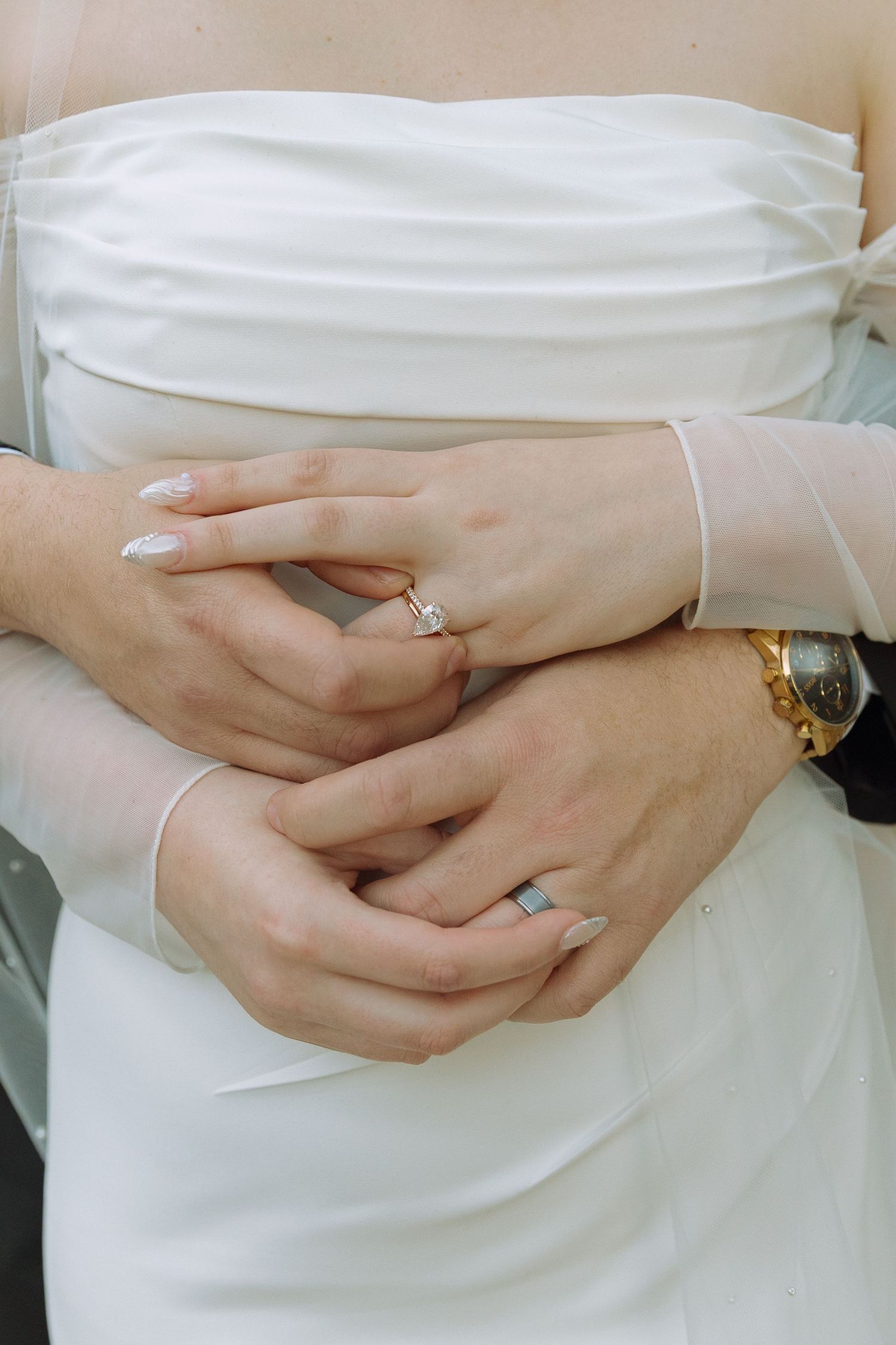 Close-up view of hands clasped together showing a sparkling engagement ring against a white dress.