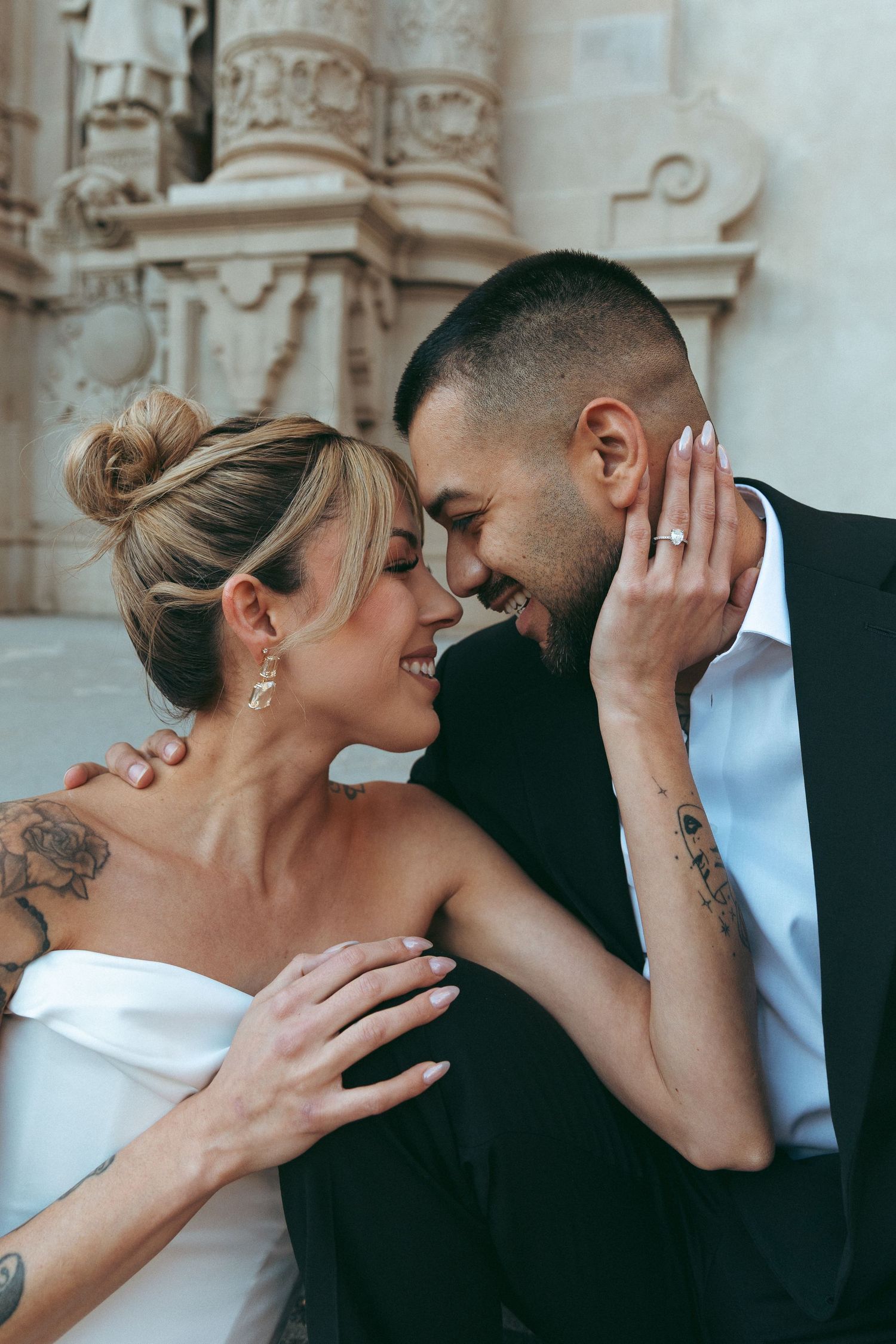 Intimate moment between newlyweds on stone steps with classical columns in background.