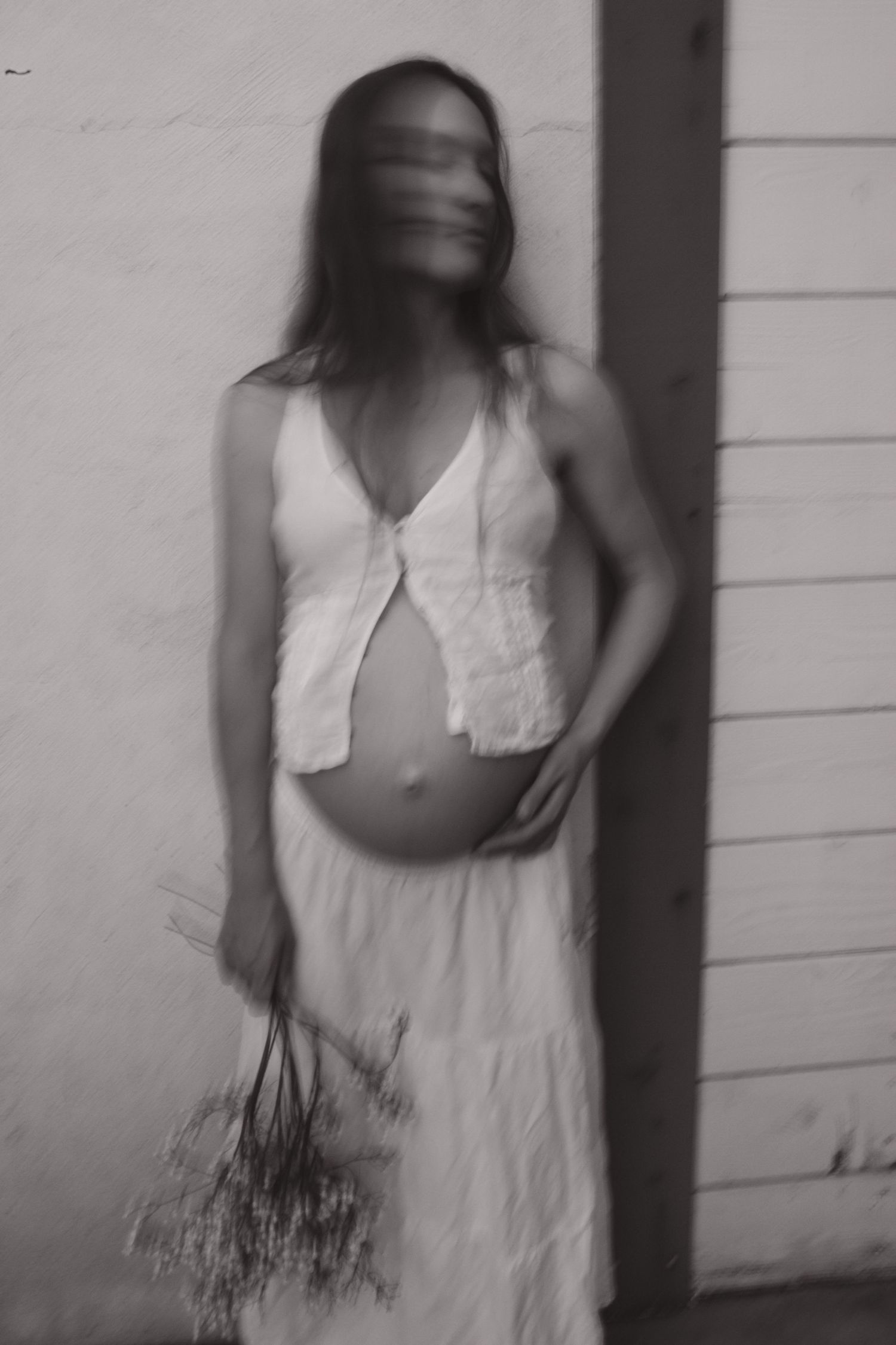 Artistic black and white portrait showing motion blur and white summer clothing against a light wall.