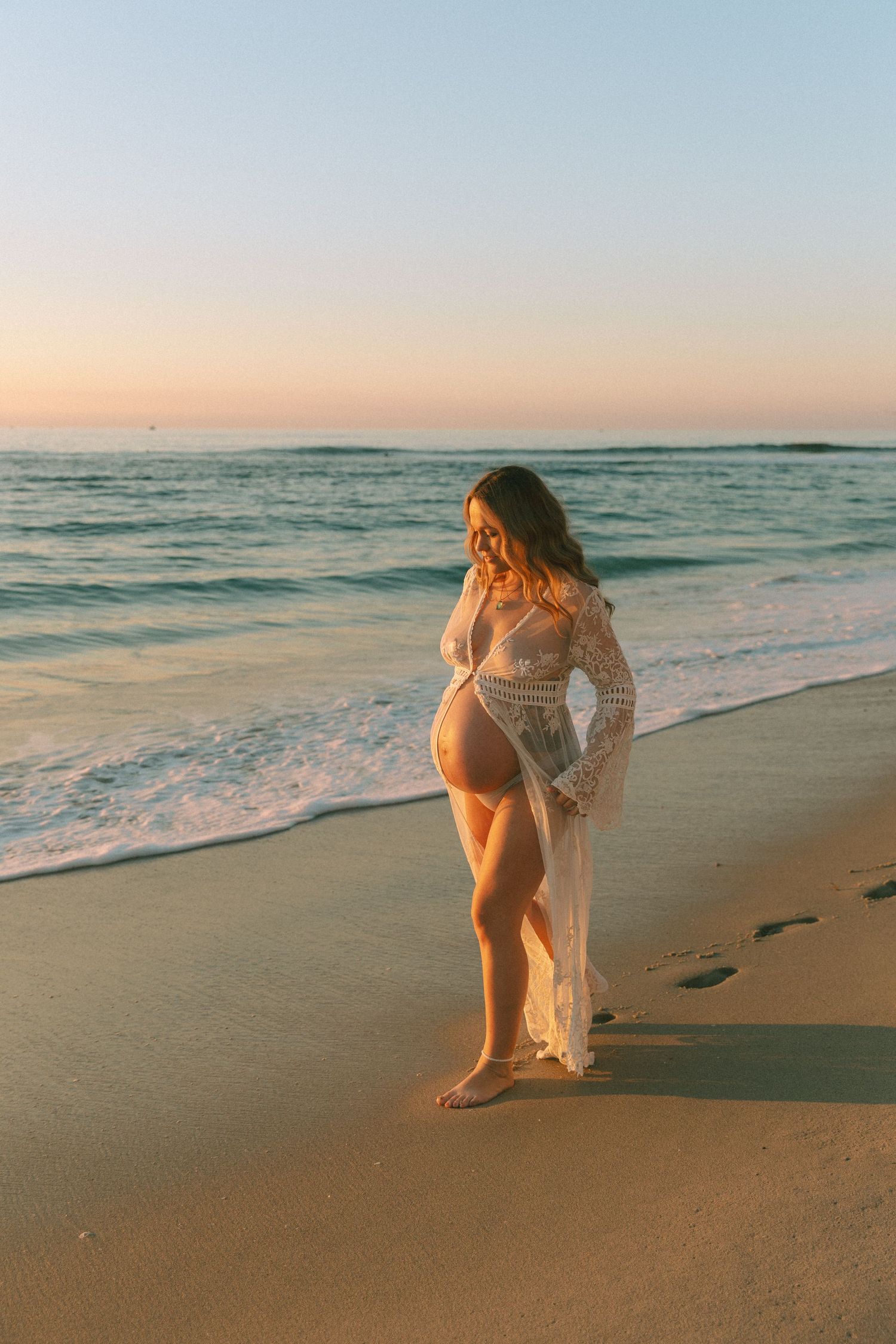 Maternity beach photoshoot with flowing sheer dress at sunset.