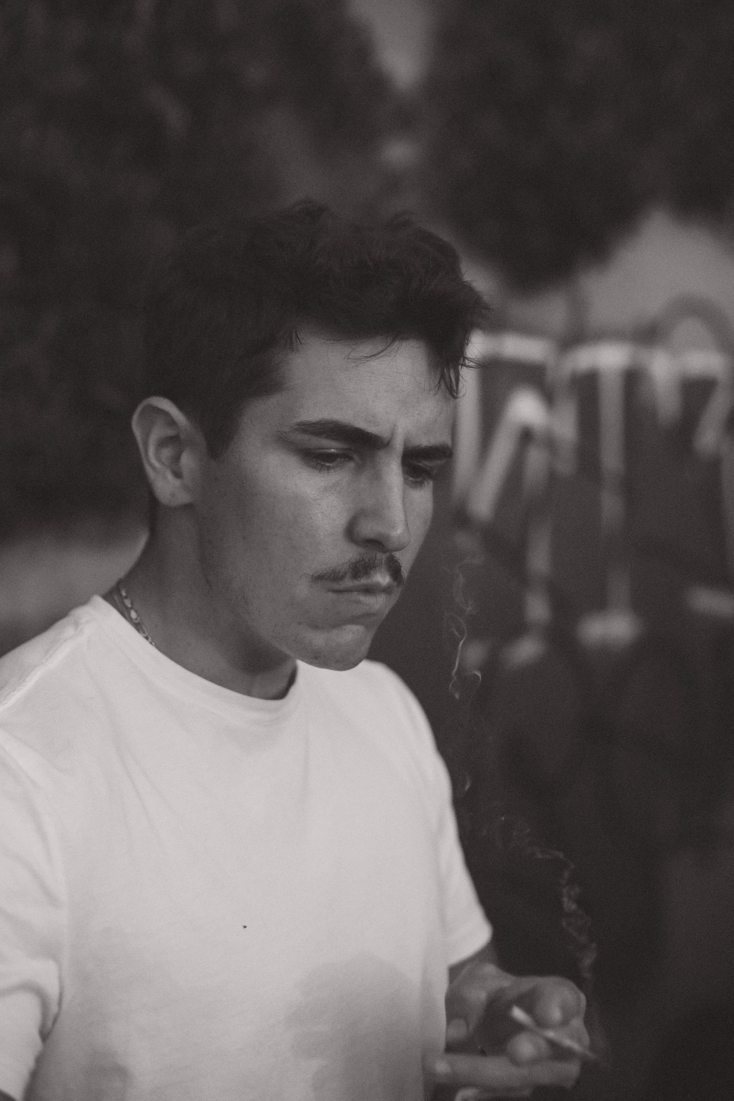A black and white portrait of a person smoking while wearing a white t-shirt.