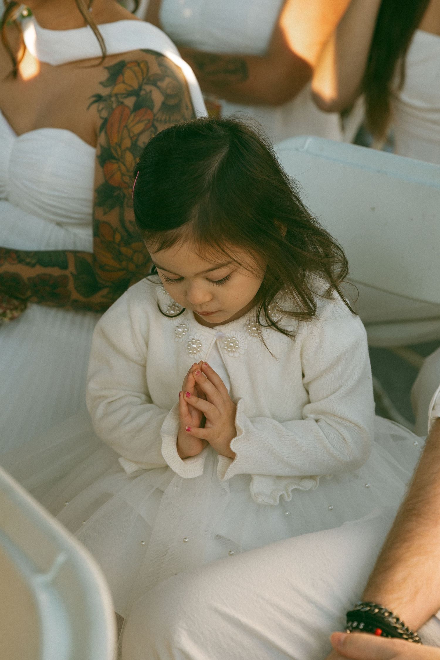 Person in white dress sitting quietly during wedding ceremony.