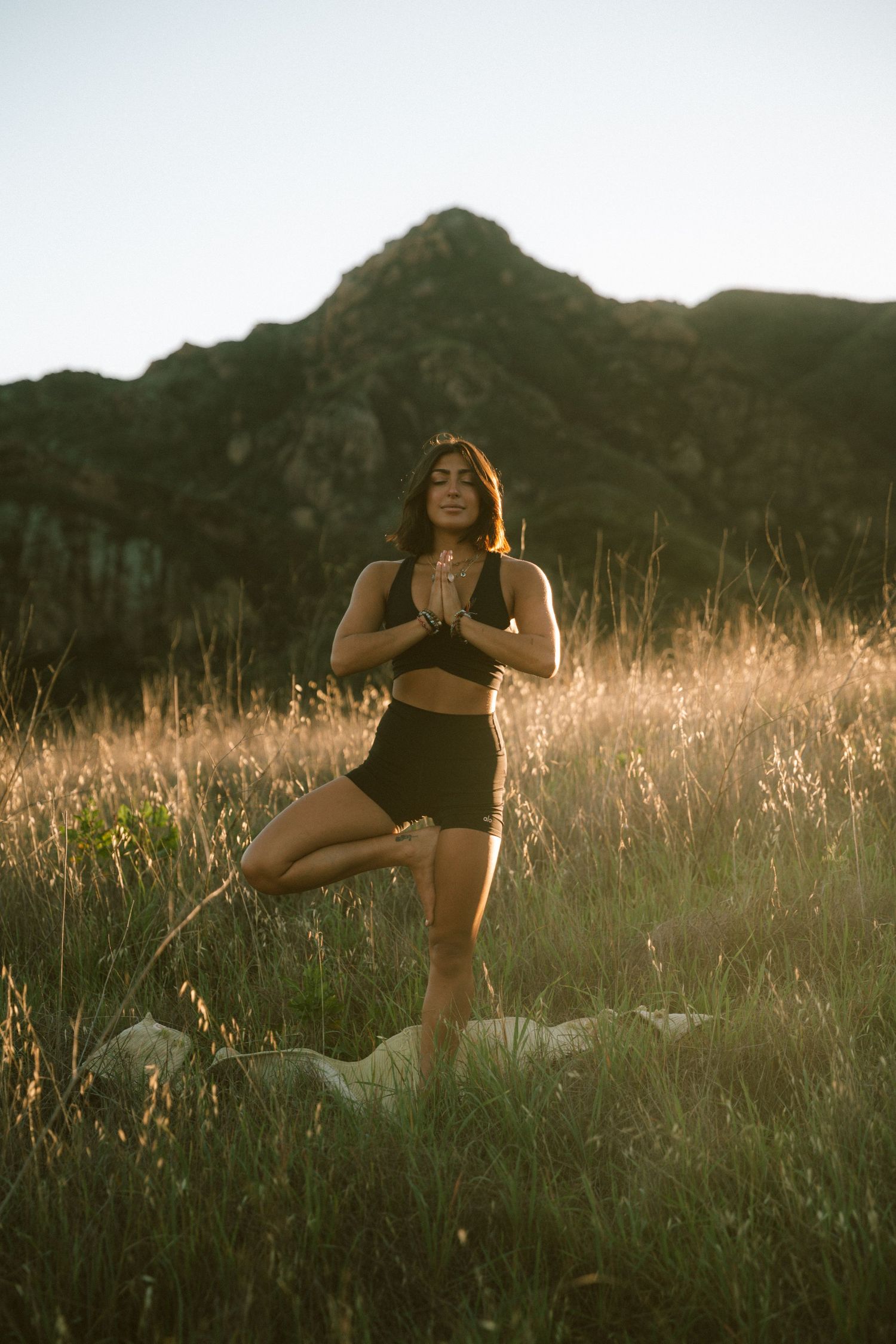 Dancer performing graceful movements in athletic wear against golden sunset and mountain backdrop.