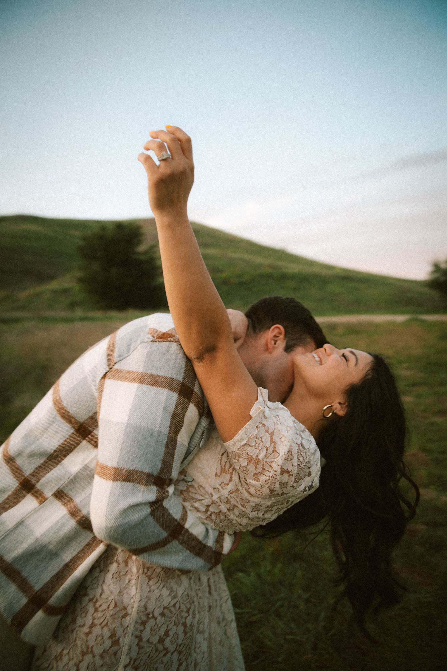 A romantic dance dip pose with a couple in formal wear against a scenic hillside.