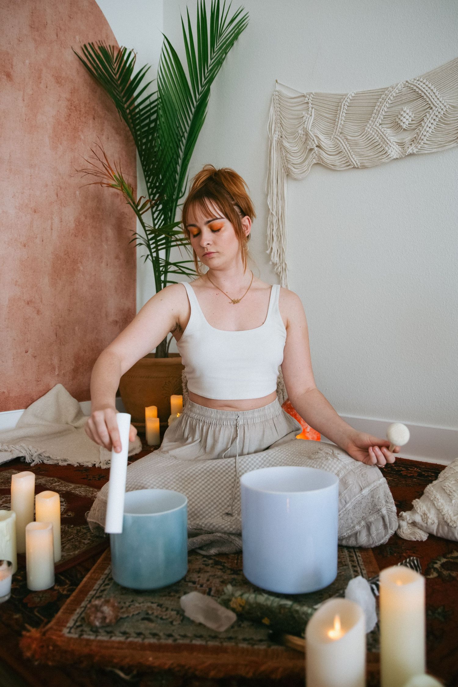 Peaceful meditation setup with blue bowls and white candles surrounded by plants and macrame decor.