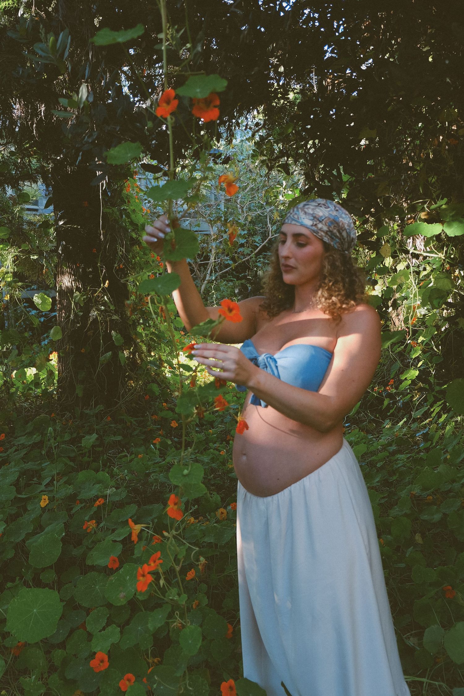Garden maternity portrait among orange flowers and lush greenery.