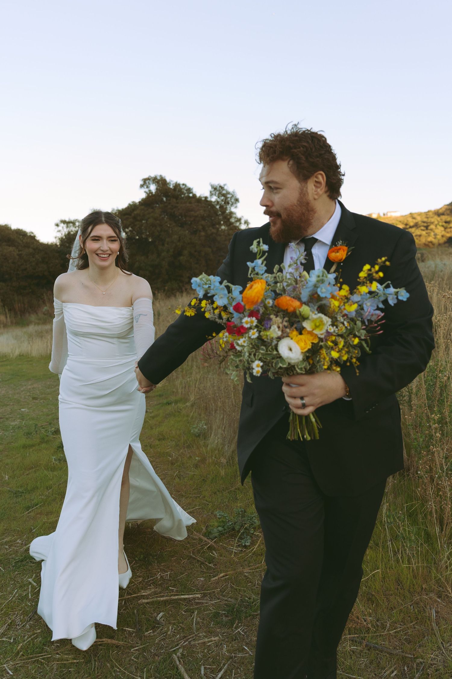 Candid shot of bride and groom walking outdoors with colorful wildflower bouquet.